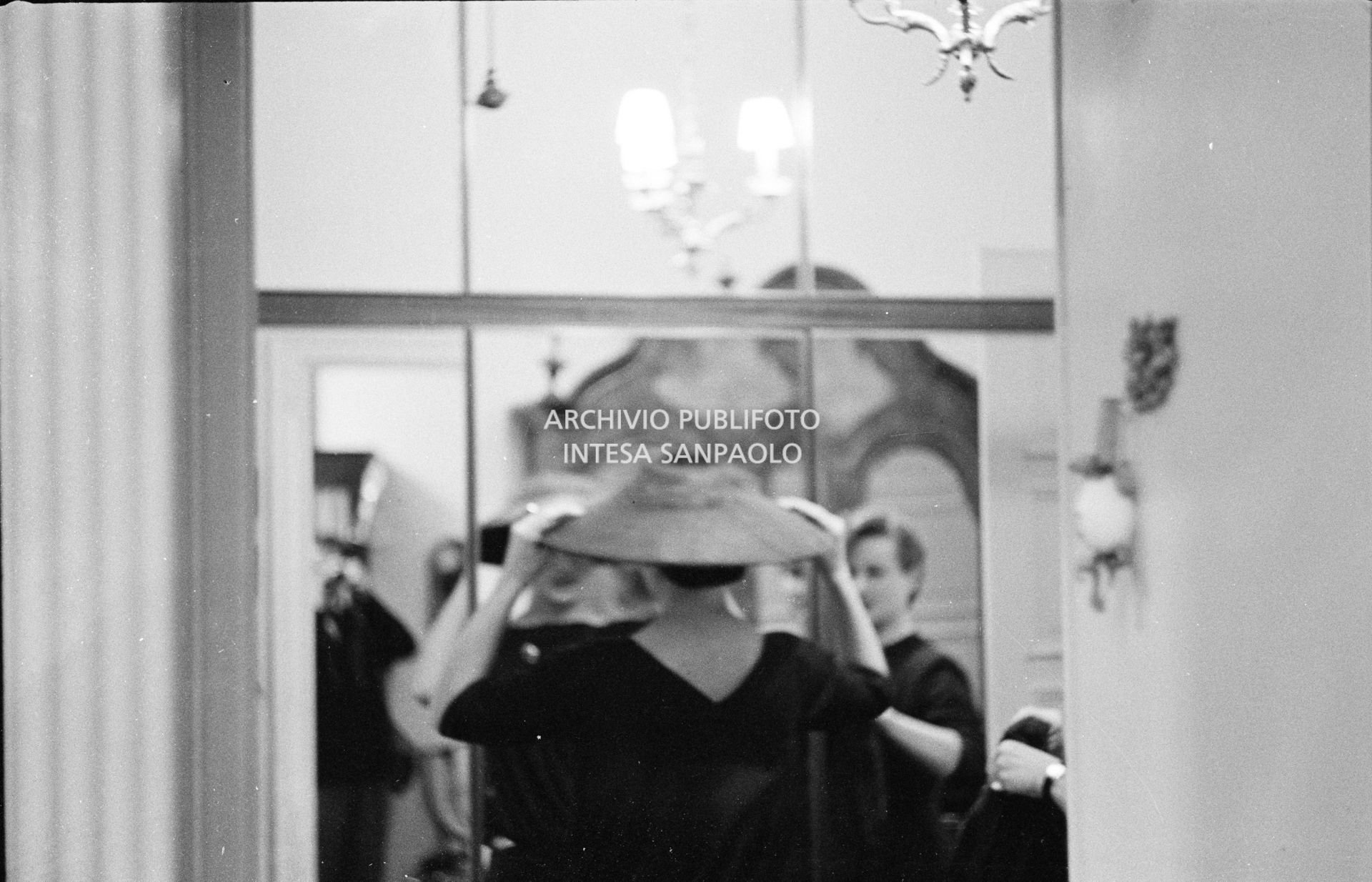 Maria Callas, ritratta nella sua abitazione, si sistema allo specchio il cappello della sartoria Biki