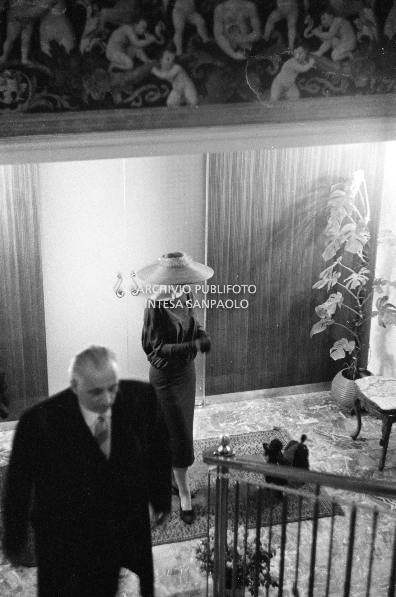 Maria Callas, ritratta nella sua abitazione, indossa un abito e un cappello della sartoria Biki; in primo piano il marito Giovanni Battista Meneghini