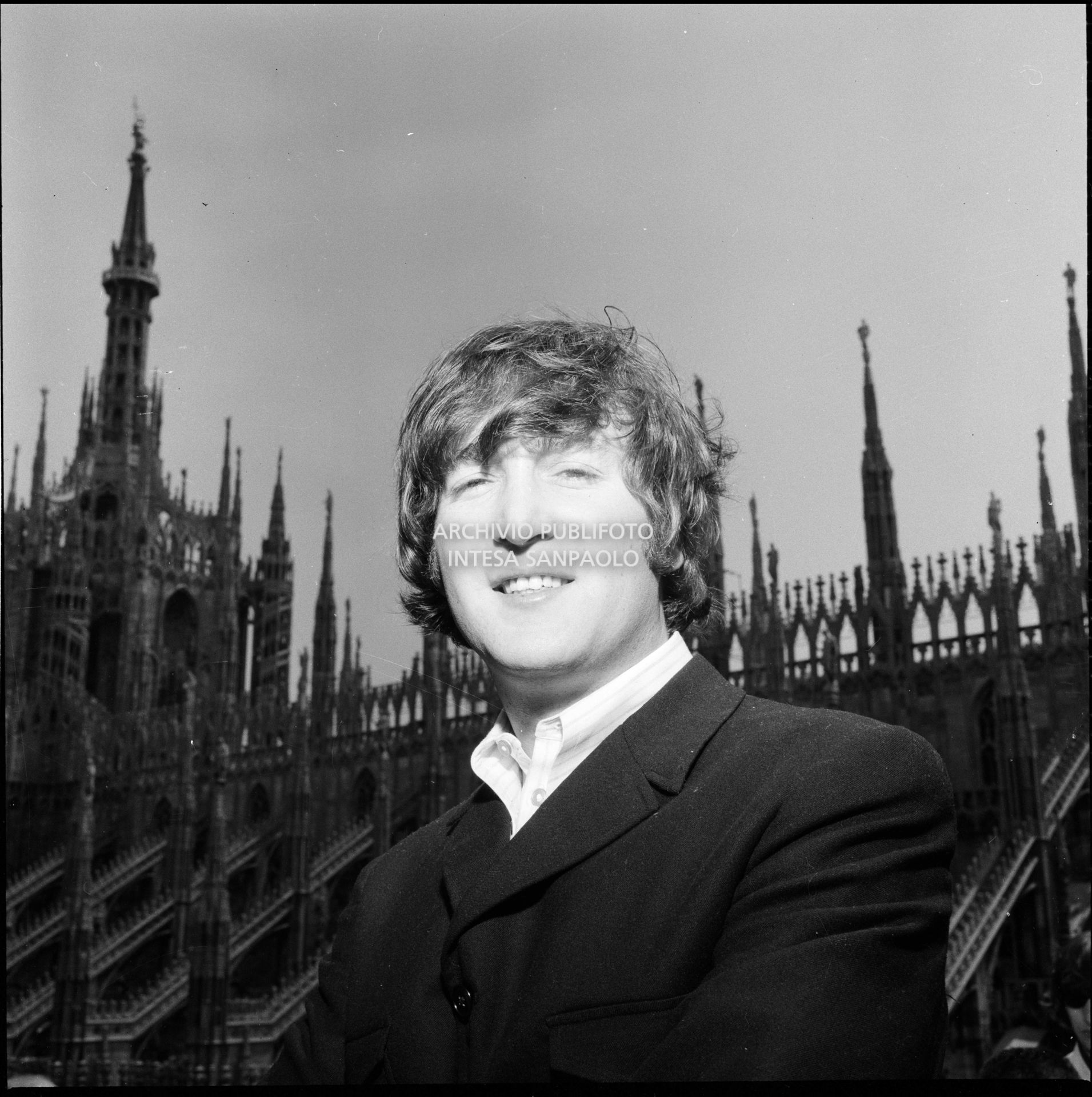 John Lennon ritratto sulla terrazza del Grand Hotel Duomo a Milano; sullo sfondo le guglie della cattedrale