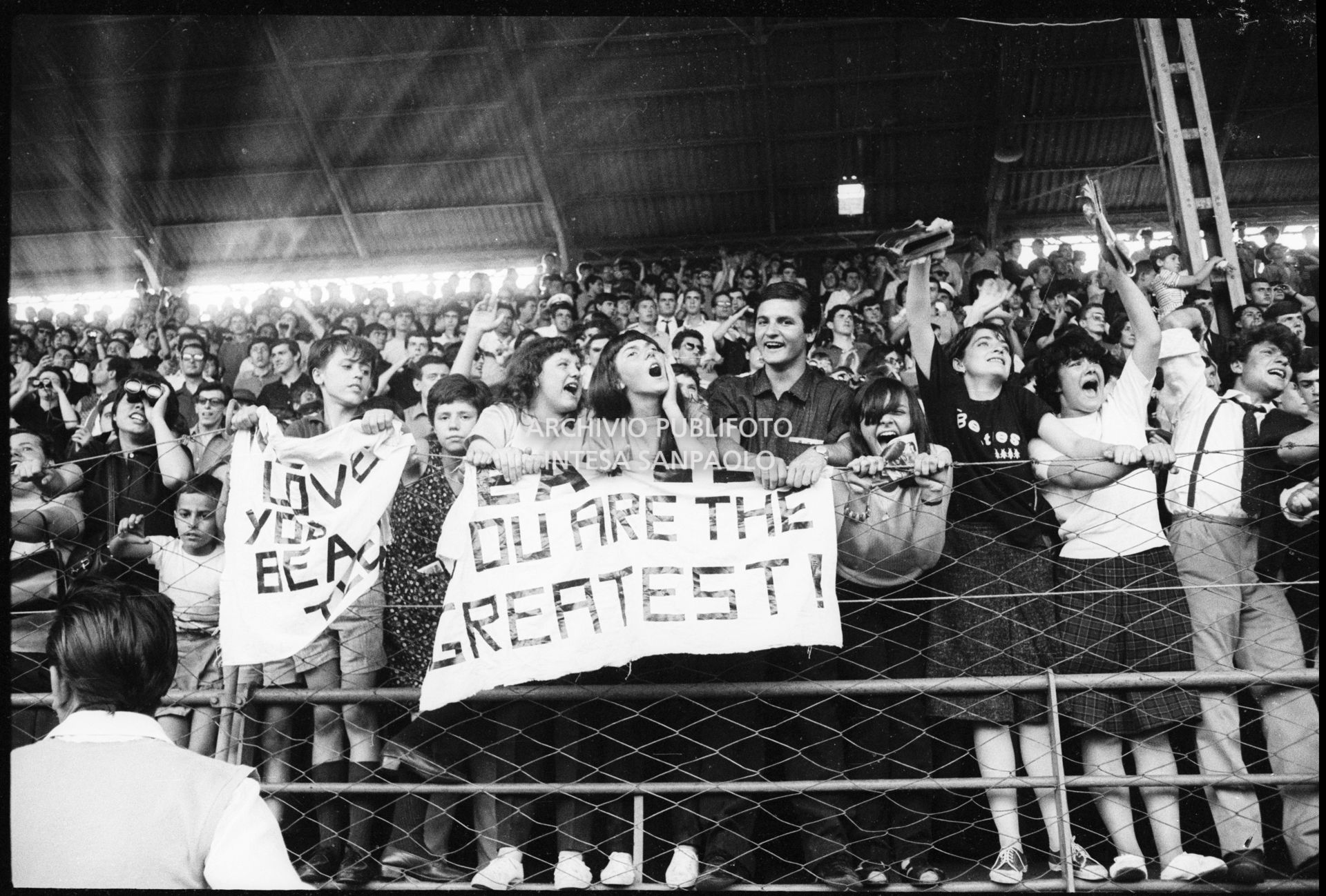 Fan scatenati sugli spalti al concerto pomeridiano dei Beatles al Vigorelli di Milano esibiscono cartelli con scritte "I love you Beatles" e "Beatles you are the greatest"
