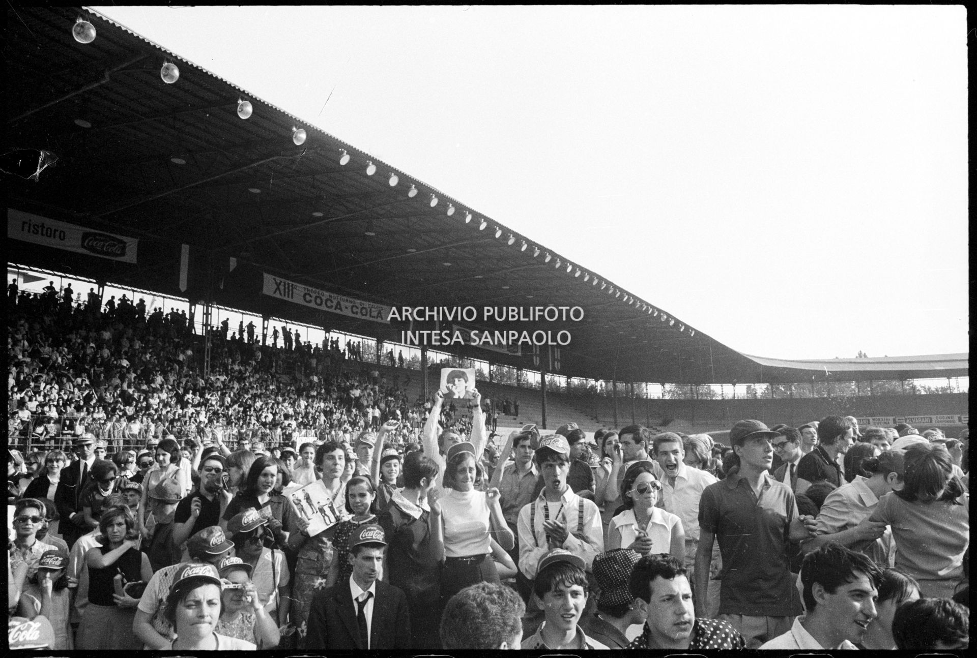 Pubblico al concerto pomeridiano dei Beatles al Vigorelli di Milano; un ragazzo mostra una fotografia di Paul McCartney