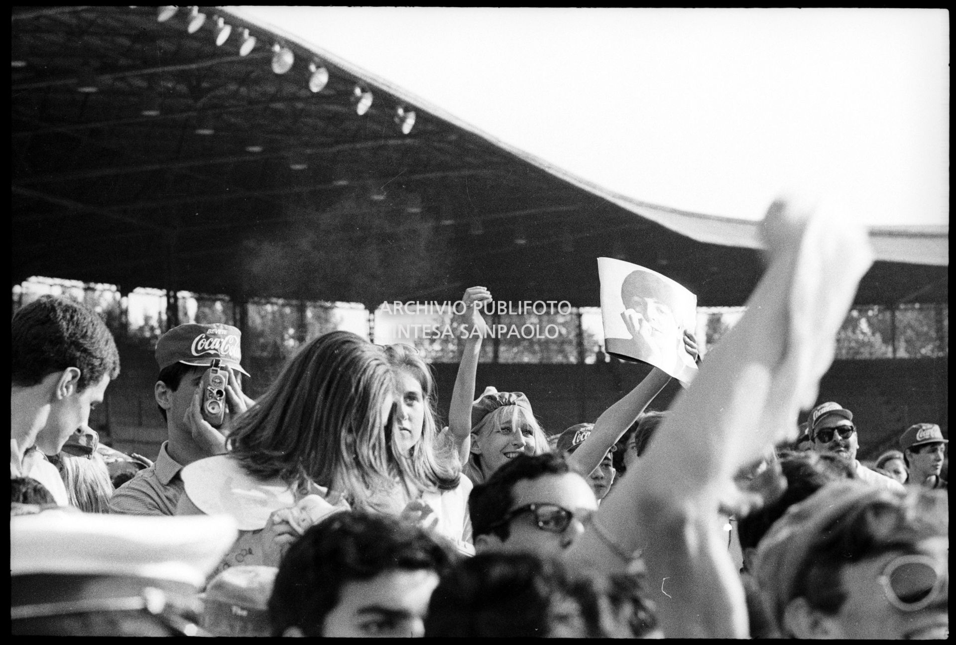 Fan scatenati al concerto pomeridiano dei Beatles al Vigorelli di Milano: una ragazza mostra una fotografia di Paul McCartney