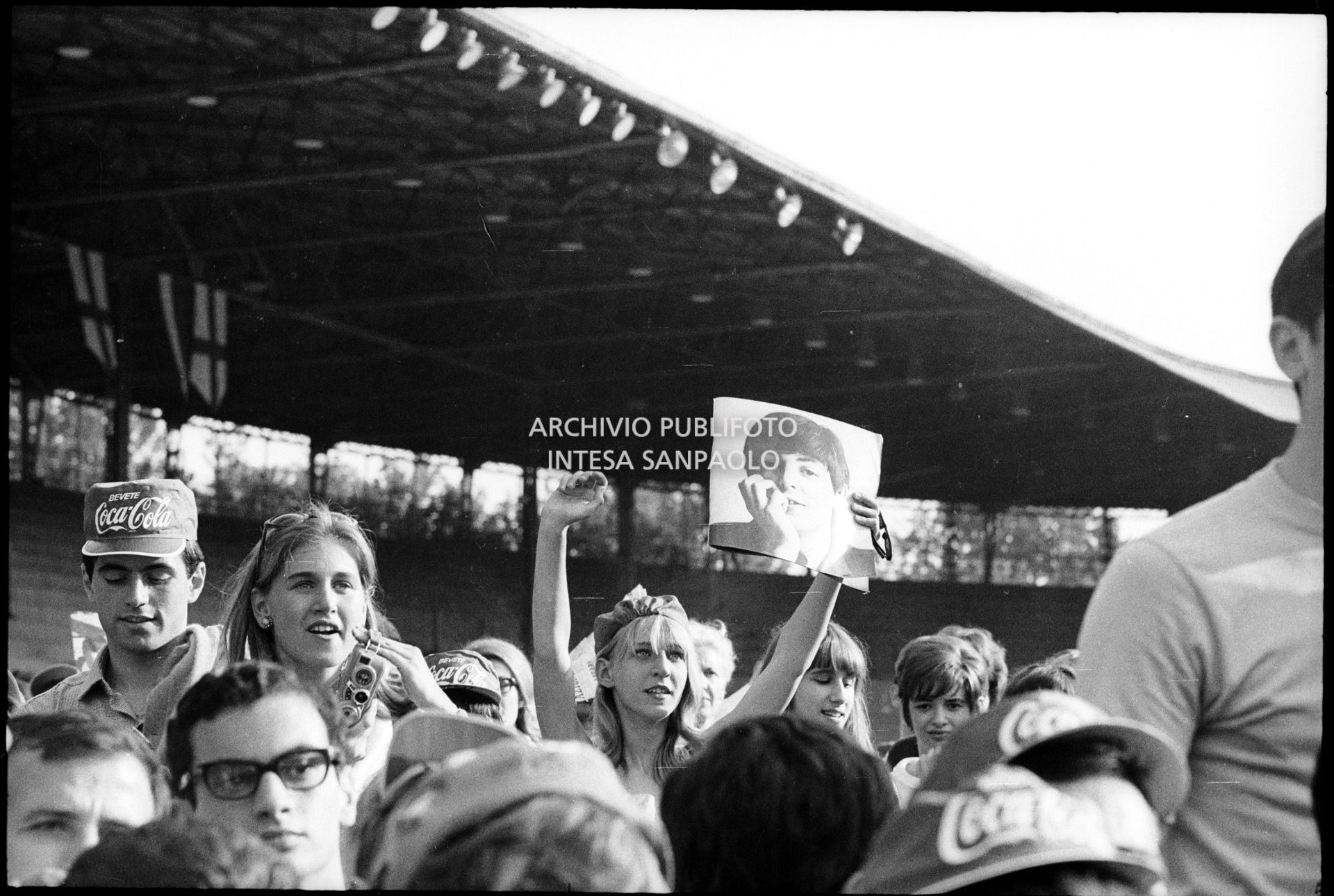 Fan scatenati al concerto pomeridiano dei Beatles al Vigorelli di Milano: una ragazza mostra una fotografia di Paul McCartney