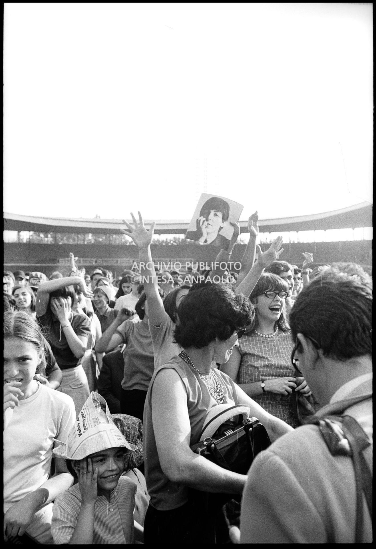 Fan scatenati al concerto pomeridiano dei Beatles al Vigorelli di Milano: una ragazza mostra una fotografia di Paul McCartney