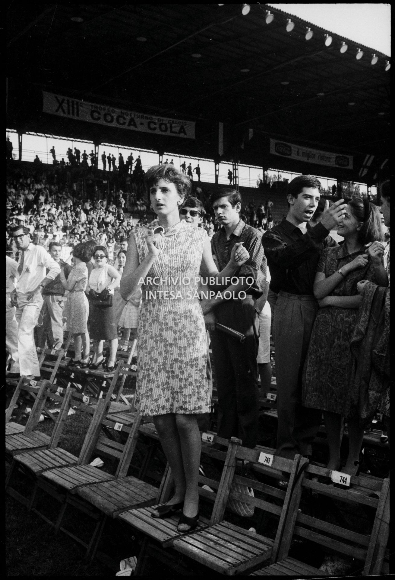 Pubblico in piedi sulle sedie al concerto pomeridiano dei Beatles al Vigorelli di Milano: in primo piano una ragazza balla