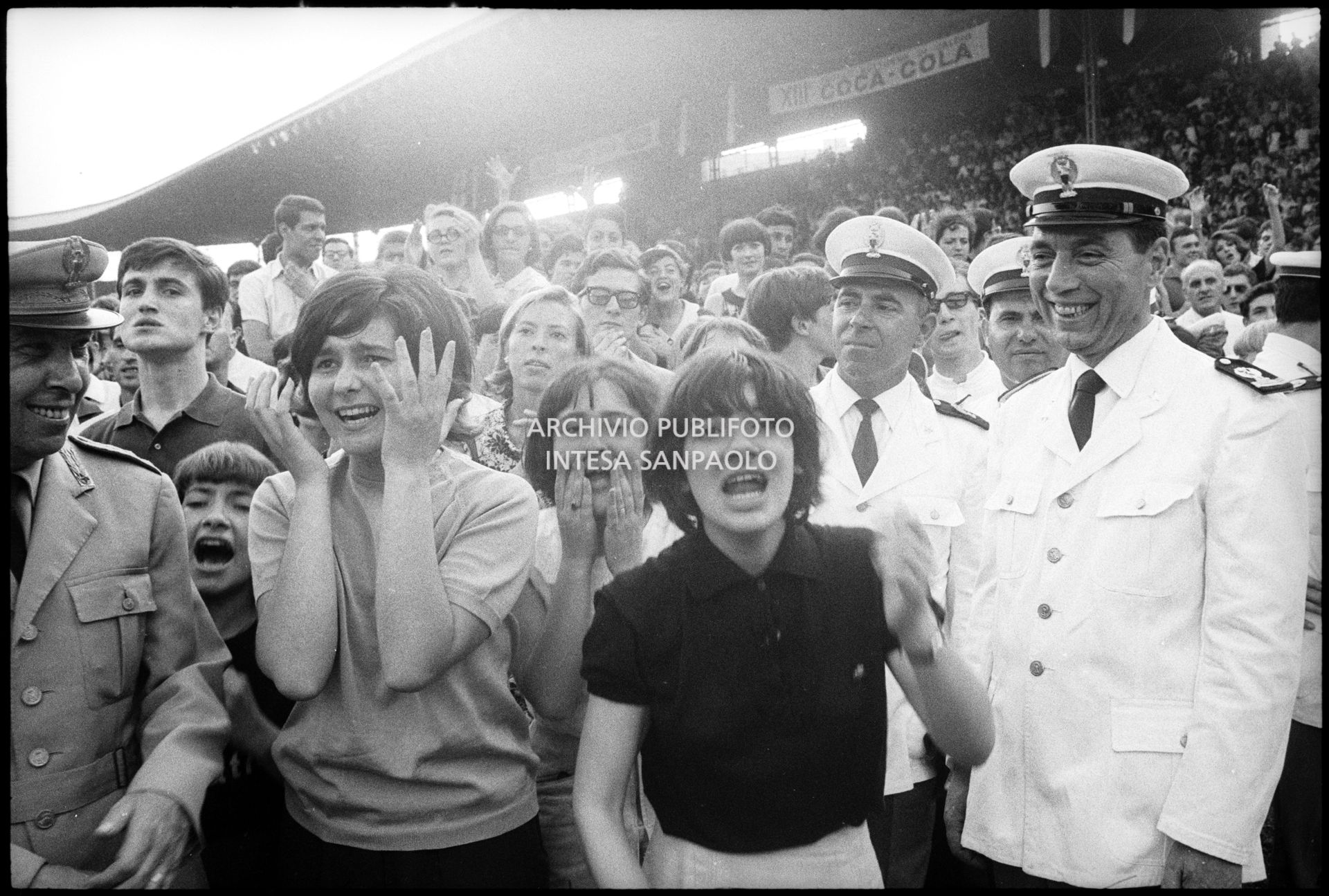Ragazze, tra il pubblico al concerto pomeridiano dei Beatles al Vigorelli di Milano, urlano per l'entusiasmo; i poliziotti della sicurezza sorridono divertiti