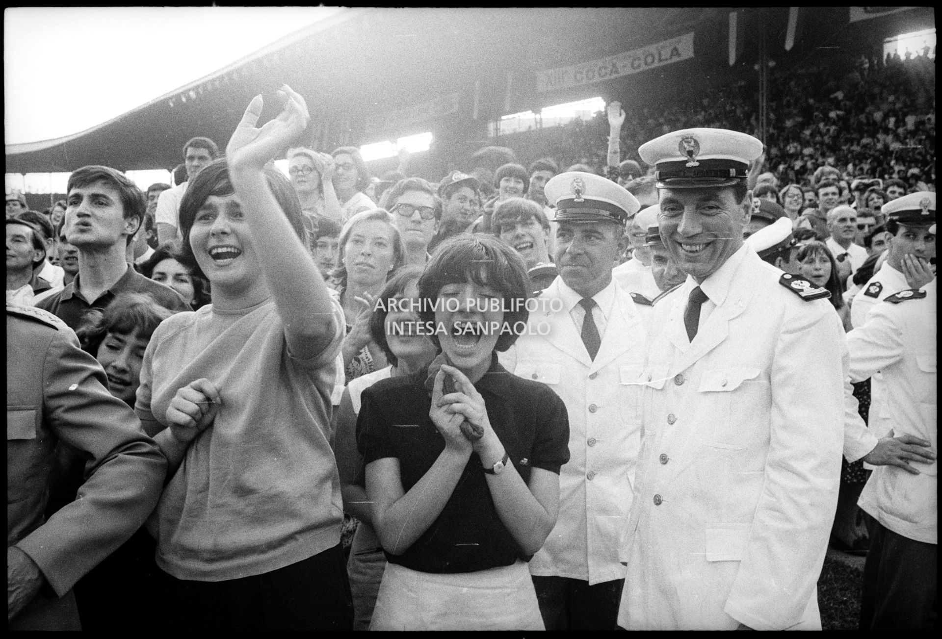 Ragazze, tra il pubblico al concerto pomeridiano dei Beatles al Vigorelli di Milano, urlano per l'entusiasmo; i poliziotti della sicurezza sorridono divertiti
