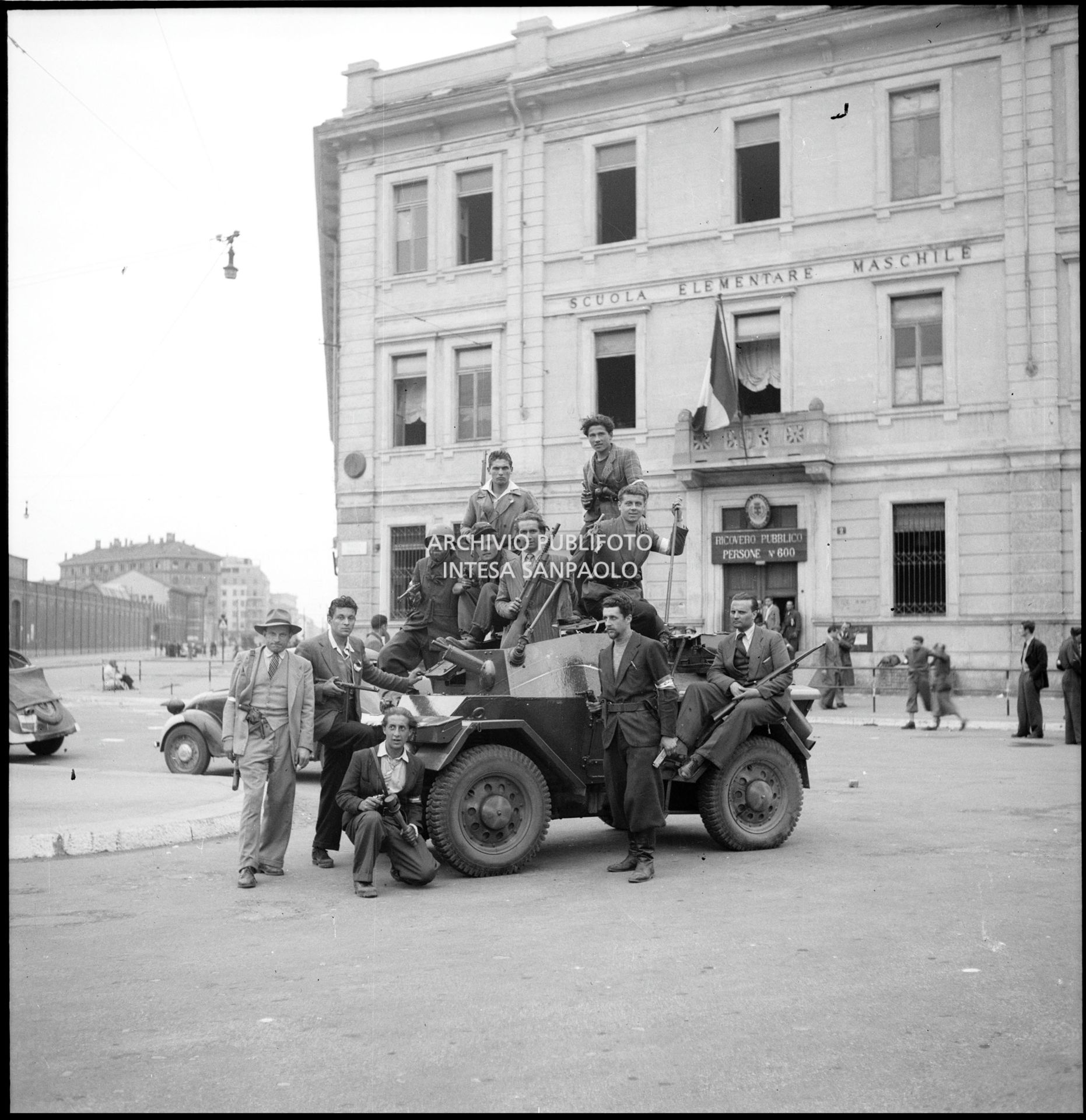 Membri del C.V.L. (Corpo Volontari della Libertà) a bordo di una autoblindo in piazza Sicilia nella prima giornata dell'insurrezione generale a Milano; sullo sfondo la scuola elementare Nicola Bonservizi convertita in Ricovero pubblico