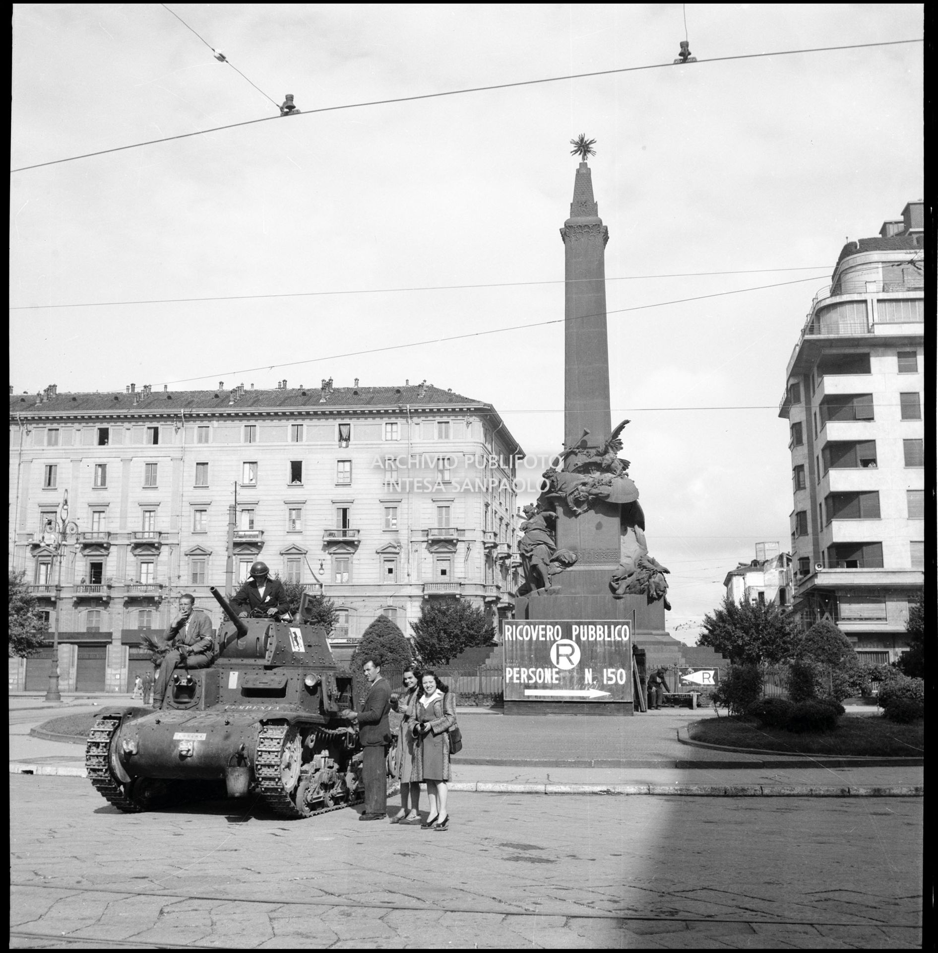 Membri del C.V.L. (Corpo Volontari della Libertà) a bordo di un carro armato M13/40, sequestrato all' Esercito Nazionale Repubblicano della RSI, in piazza Cinque Giornate a Milano nella prima giornata dell'insurrezione generale; sullo sfondo il cartello del Ricovero pubblico