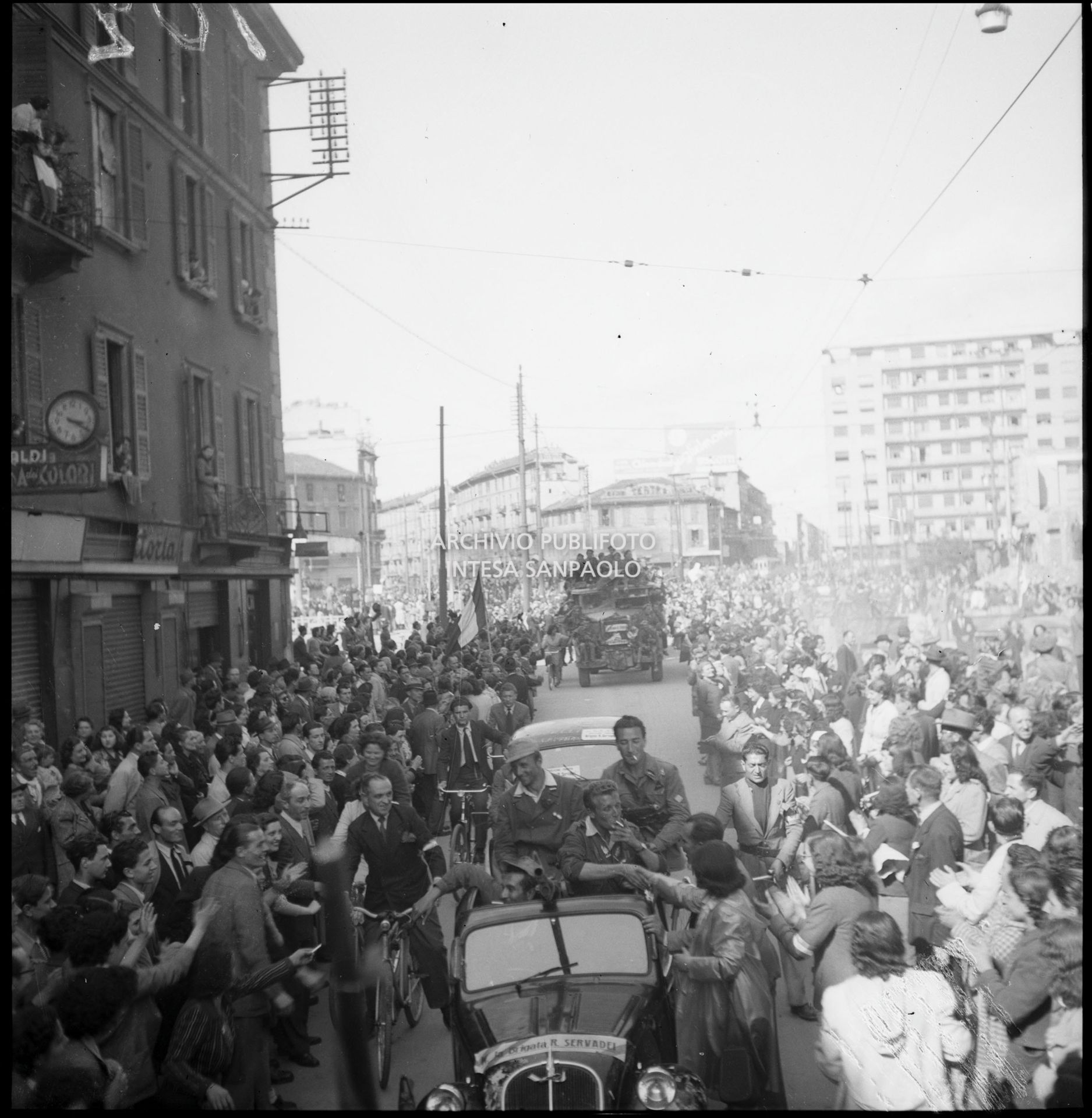 La folla festante accoglie l'ingresso a Milano delle colonne partigiane: sull'automobile in primo piano "Brigata R. Servadei"