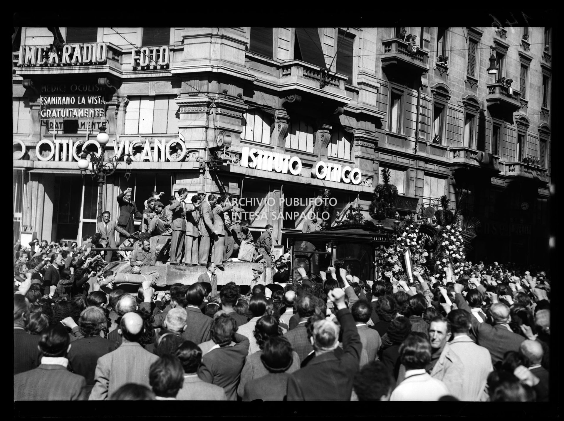 Folla con il pugno chiuso alzato accoglie il corteo funebre dei caduti durante l'insurrezione generale, che ha liberato la città, in piazza Cordusio a Milano