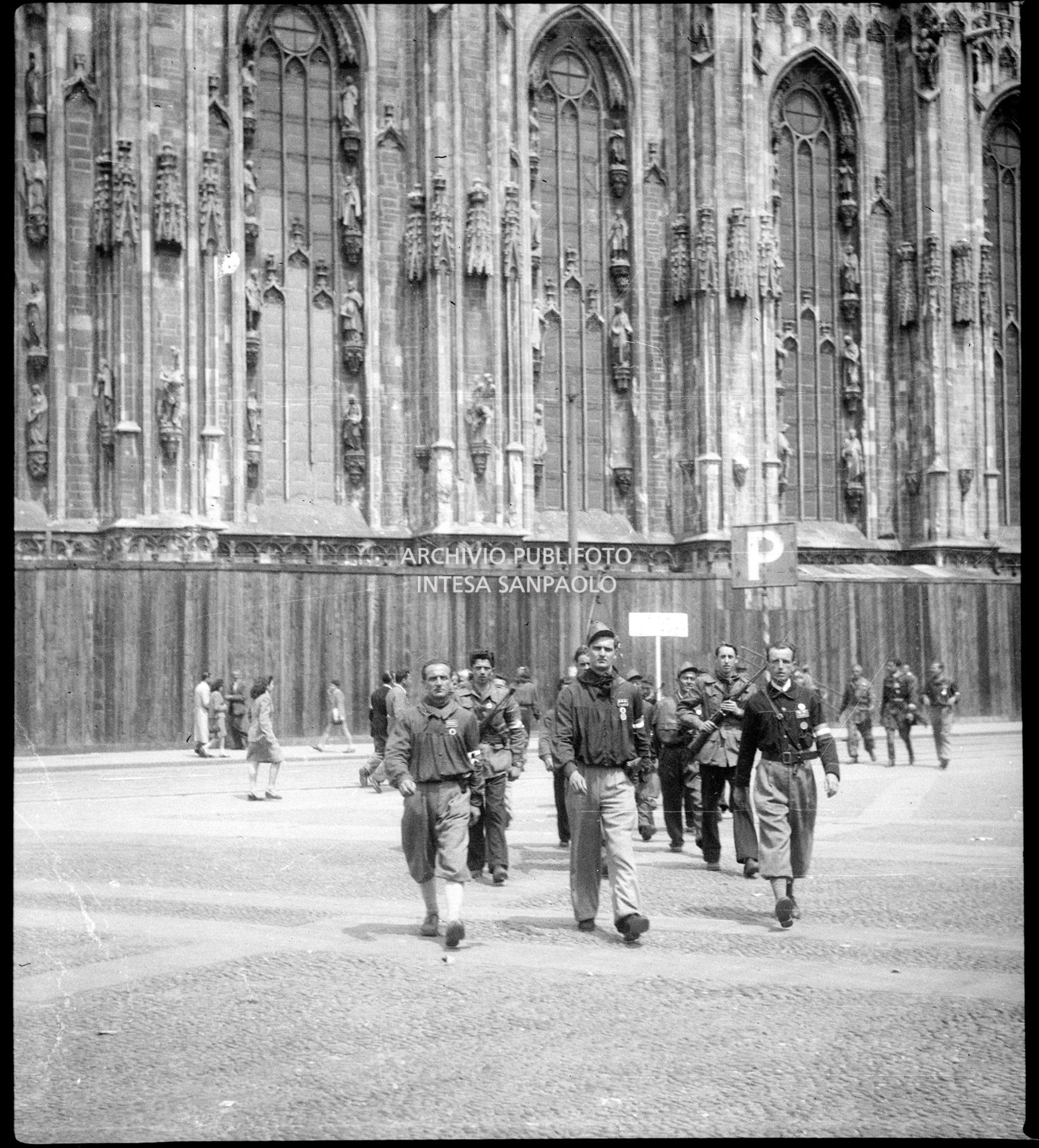 Partigiani in piazza del Duomo si avviano alla sfilata con le formazioni convenute a Milano; ai lati la folla accorsa per festeggiarle per le vie della città