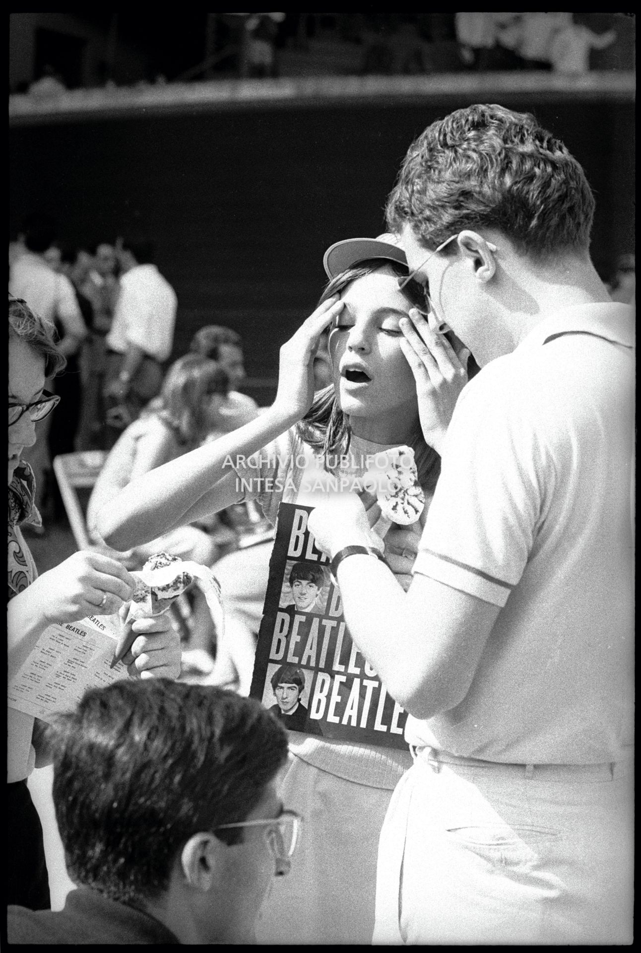 Pubblico accaldato in attesa dell'inizio del concerto pomeridiano dei Beatles al Vigorelli di Milano; una ragazza si scarta un gelato