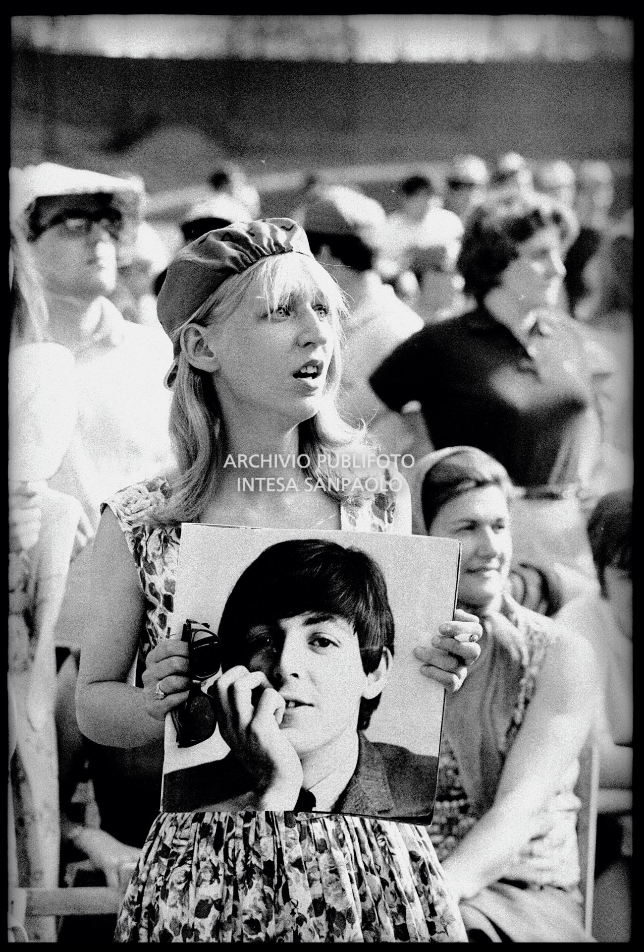 Una ragazza tra il pubblico al concerto pomeridiano dei Beatles al Vigorelli di Milano tiene in mano la fotografia di Paul McCartney