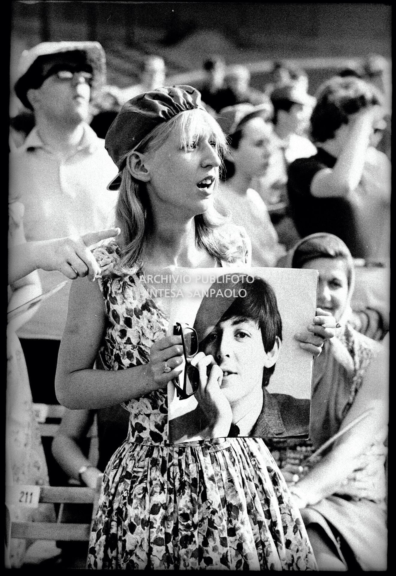 Una ragazza tra il pubblico al concerto pomeridiano dei Beatles al Vigorelli di Milano tiene in mano la fotografia di Paul McCartney
