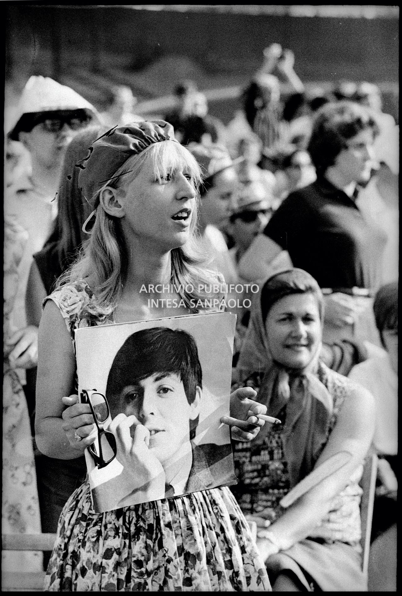 Una ragazza tra il pubblico al concerto pomeridiano dei Beatles al Vigorelli di Milano tiene in mano la fotografia di Paul McCartney
