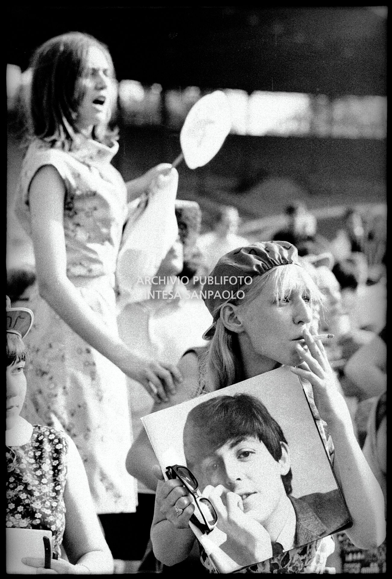 Una ragazza tra il pubblico al concerto pomeridiano dei Beatles al Vigorelli di Milano tiene in mano la fotografia di Paul McCartney