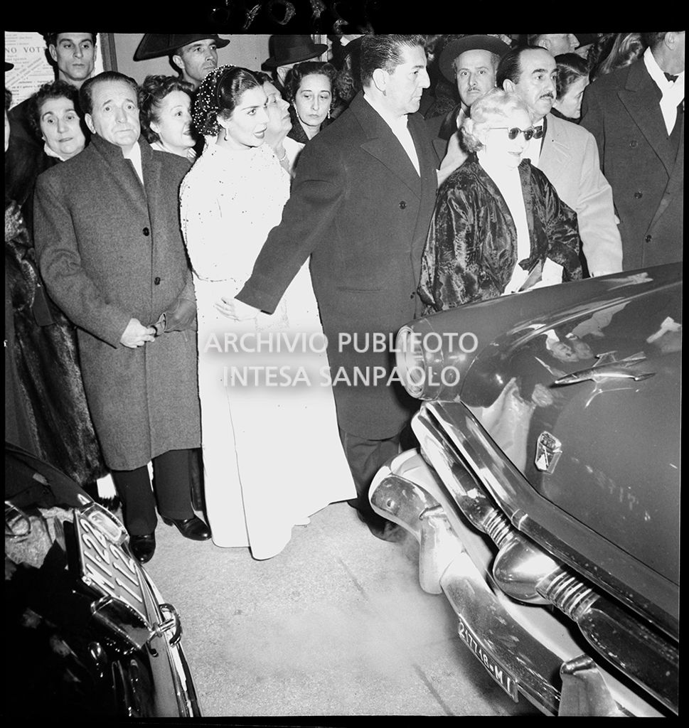 Spettatori nella galleria delle carrozze del Teatro alla Scala, in attesa delle automobili, al termine della serata inaugurale della stagione lirica 1954-1955 con l'opera "La Vestale", di Gaspare Spontini, con la regia di Luchino Visconti e diretta da Antonino Votto
