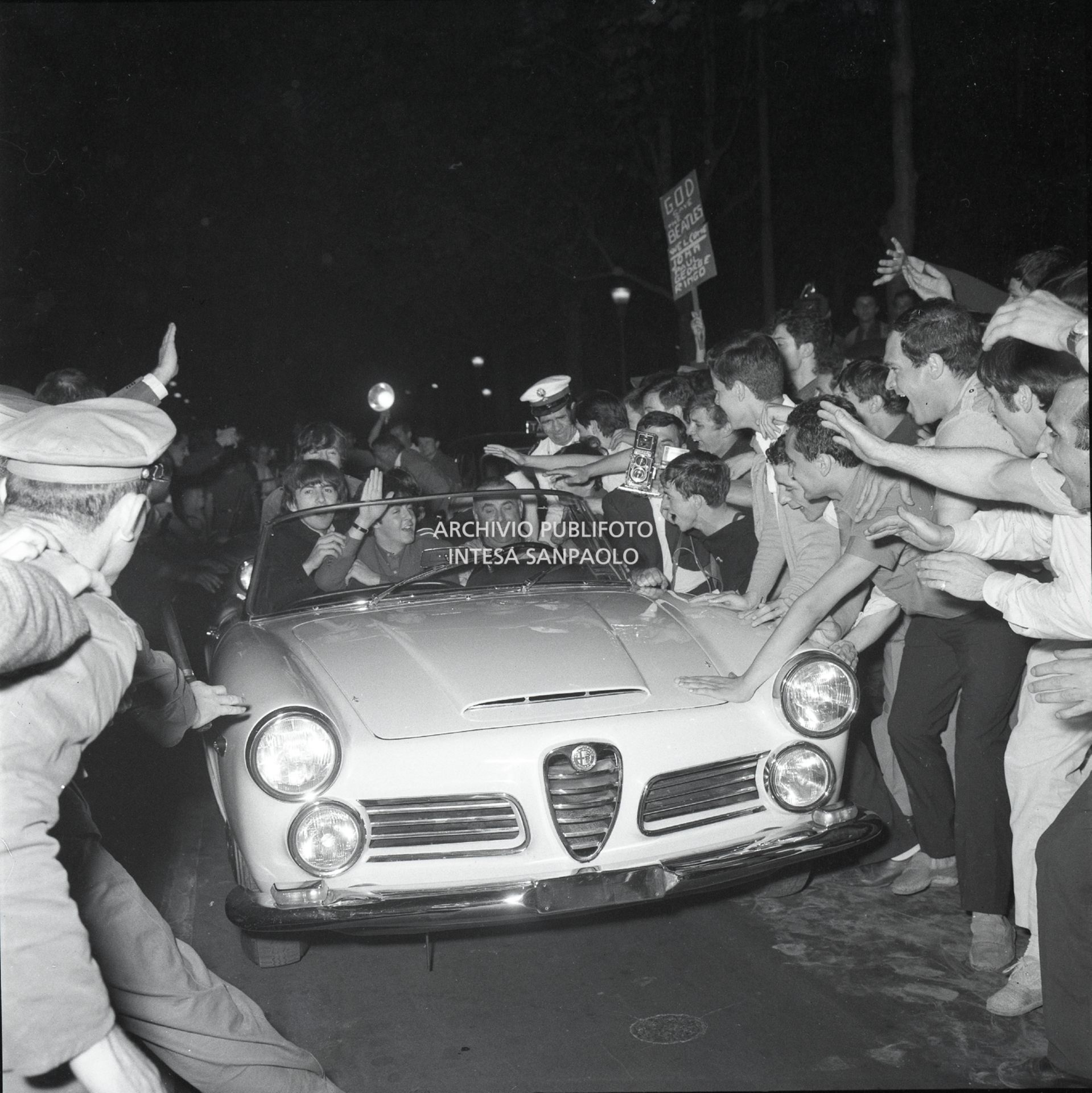 Fan in delirio per il passaggio in auto dei Beatles, a bordo di un'Alfa Romeo 2600 spider, appena arrivati alla Stazione Centrale di Milano