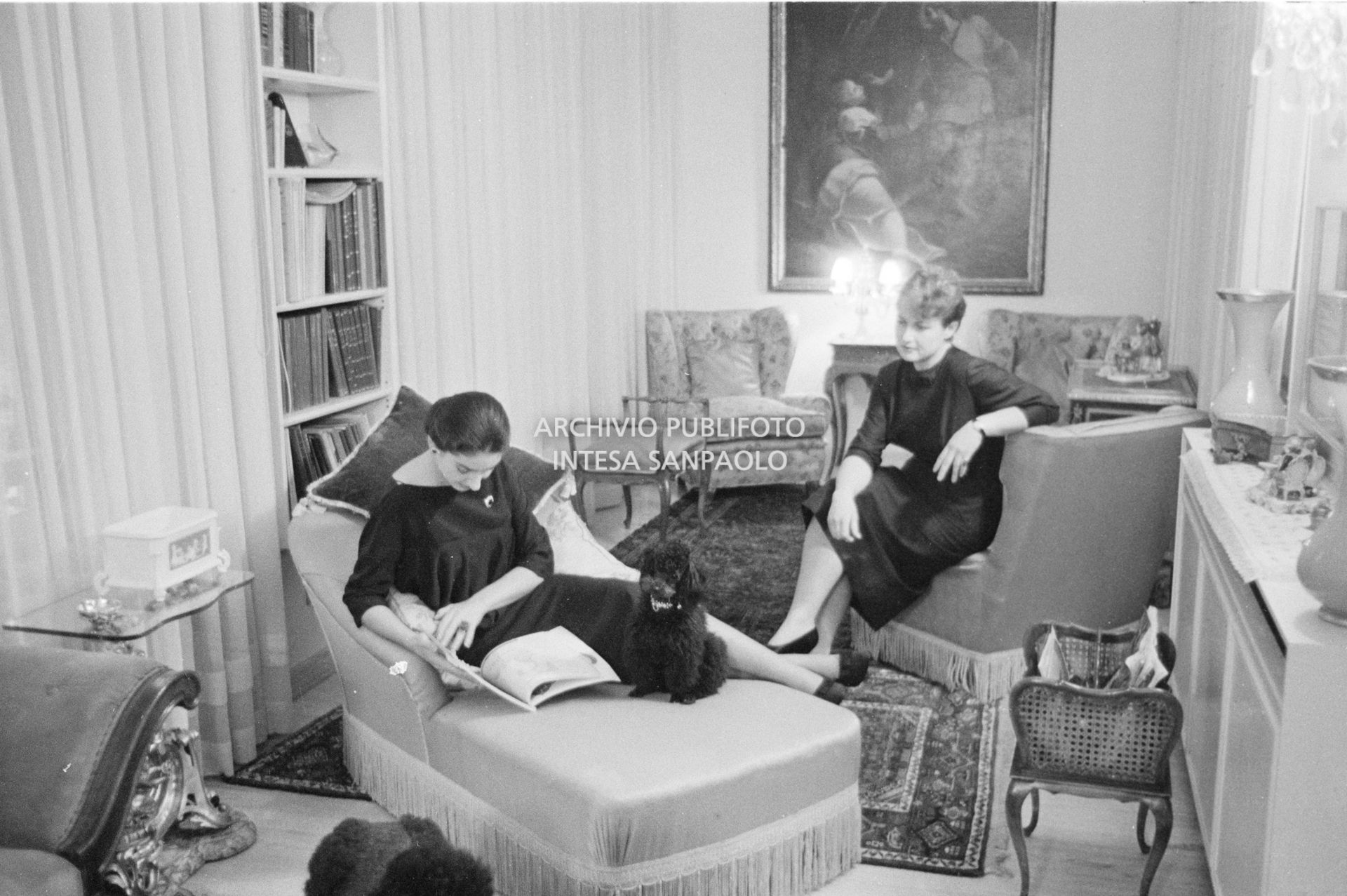 Maria Callas ritratta nella sua abitazione, seduta sulla chaise longue in salotto, mentre legge una rivista