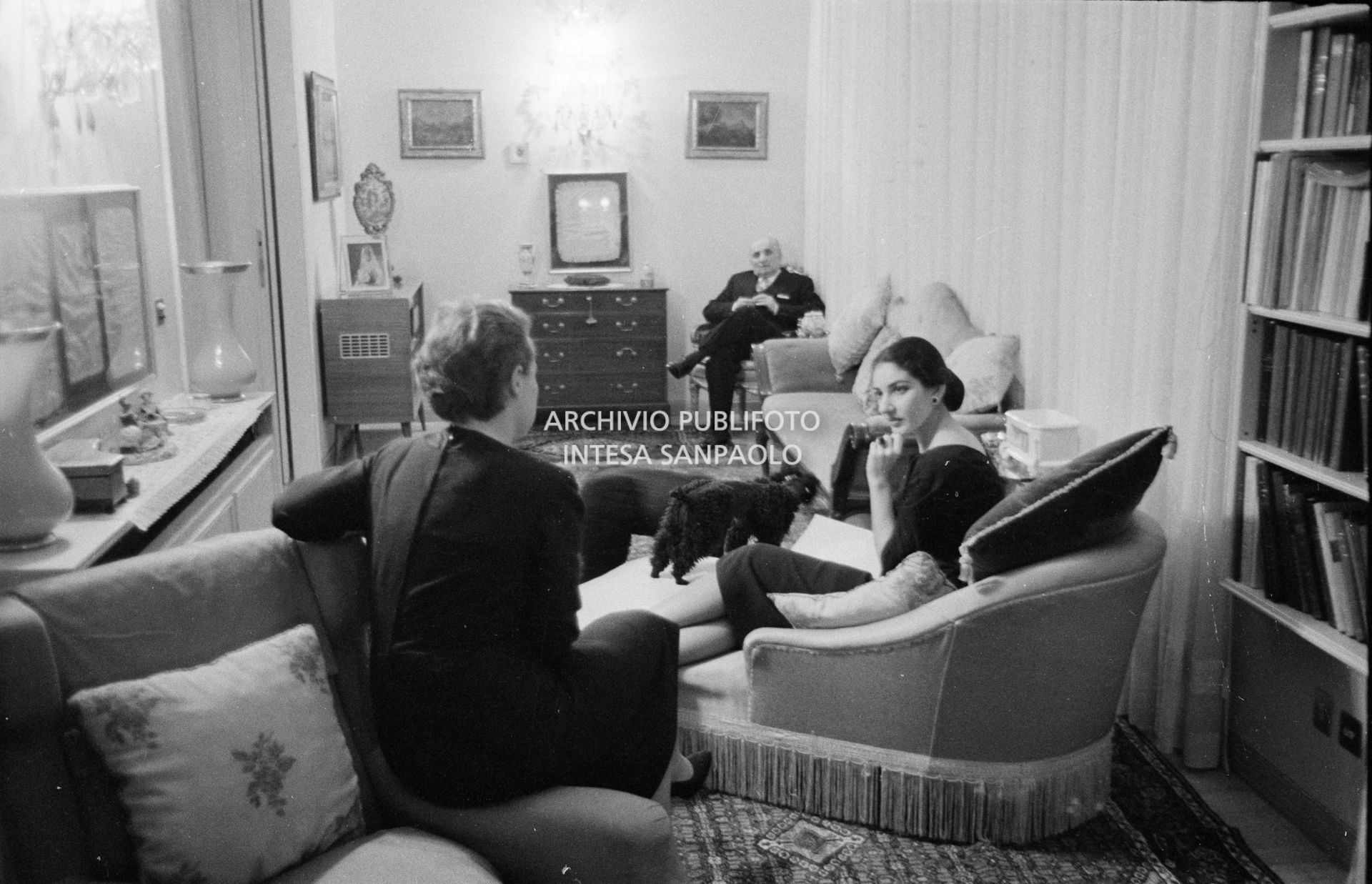 Maria Callas sulla chaise longue nel salotto di casa sua con la segretaria, il marito Gian Battista Meneghini e il suo barboncino