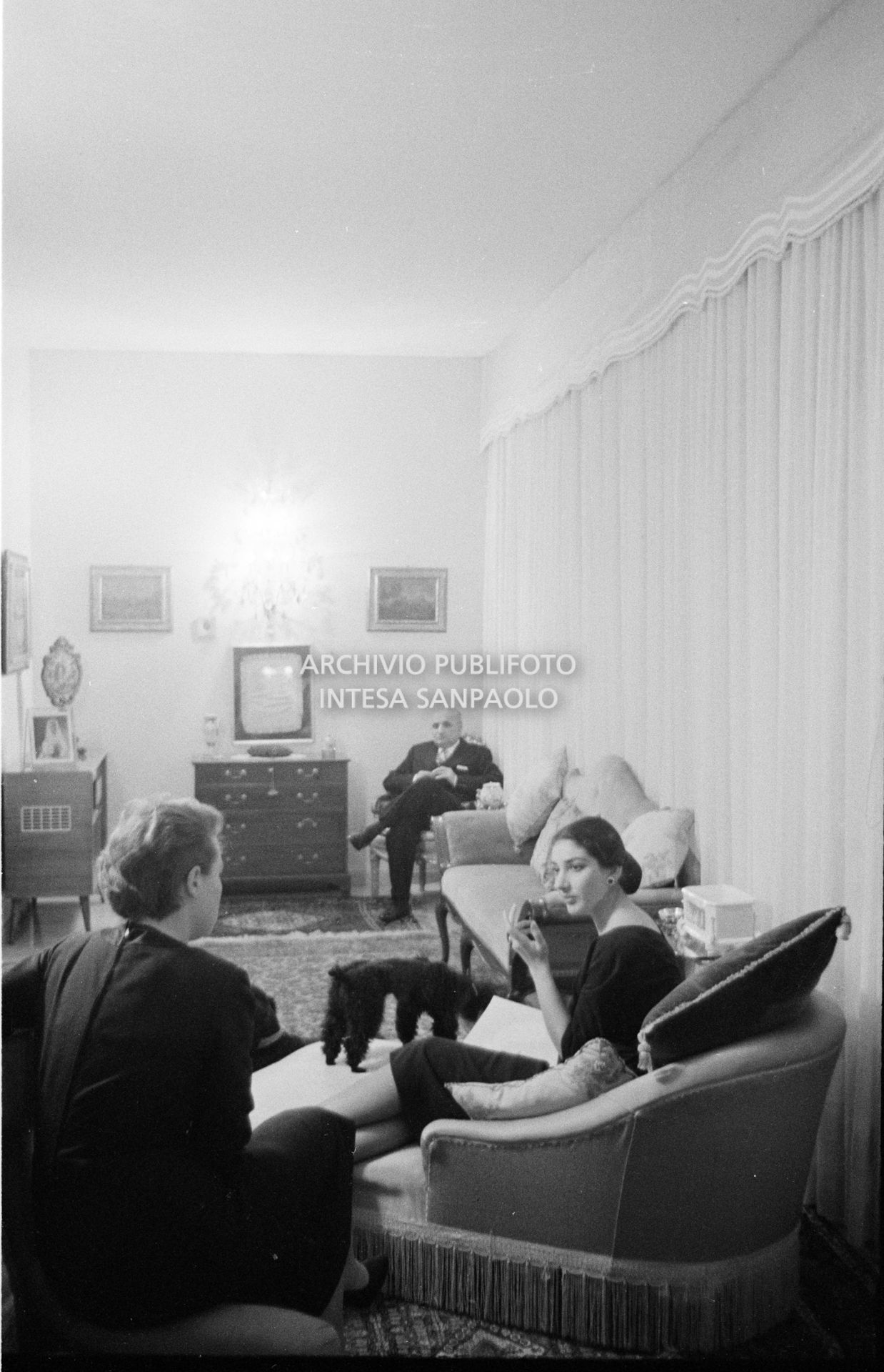 Maria Callas sulla chaise longue nel salotto di casa sua con la segretaria, il marito Gian Battista Meneghini e il suo barboncino