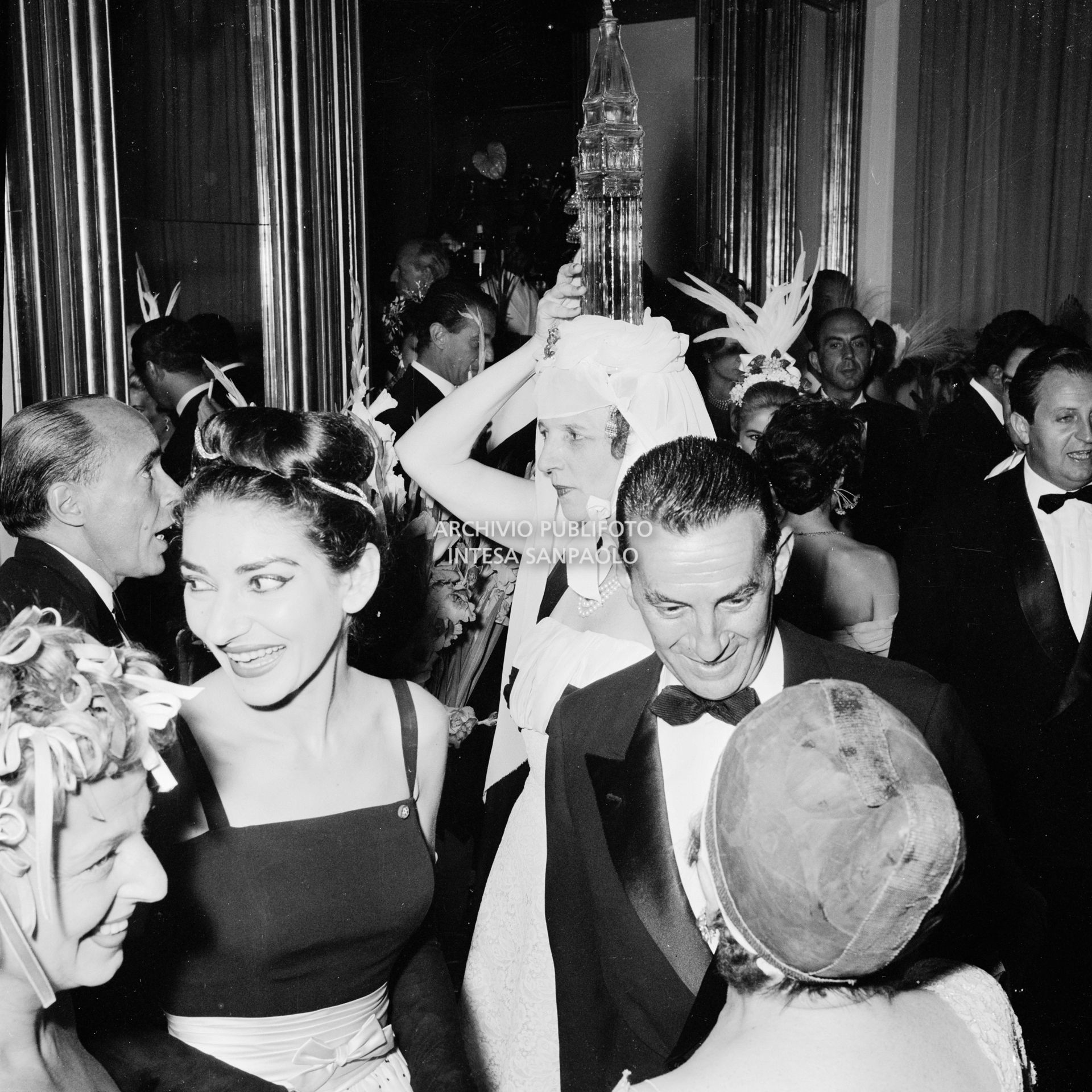 La marchesa Olga Cadaval, con la bottiglia a forma di campanile di San Marco in testa, Elsa Maxwell (di spalle), e Maria Callas, tra gli altri, al ricevimento organizzato in onore della soprano