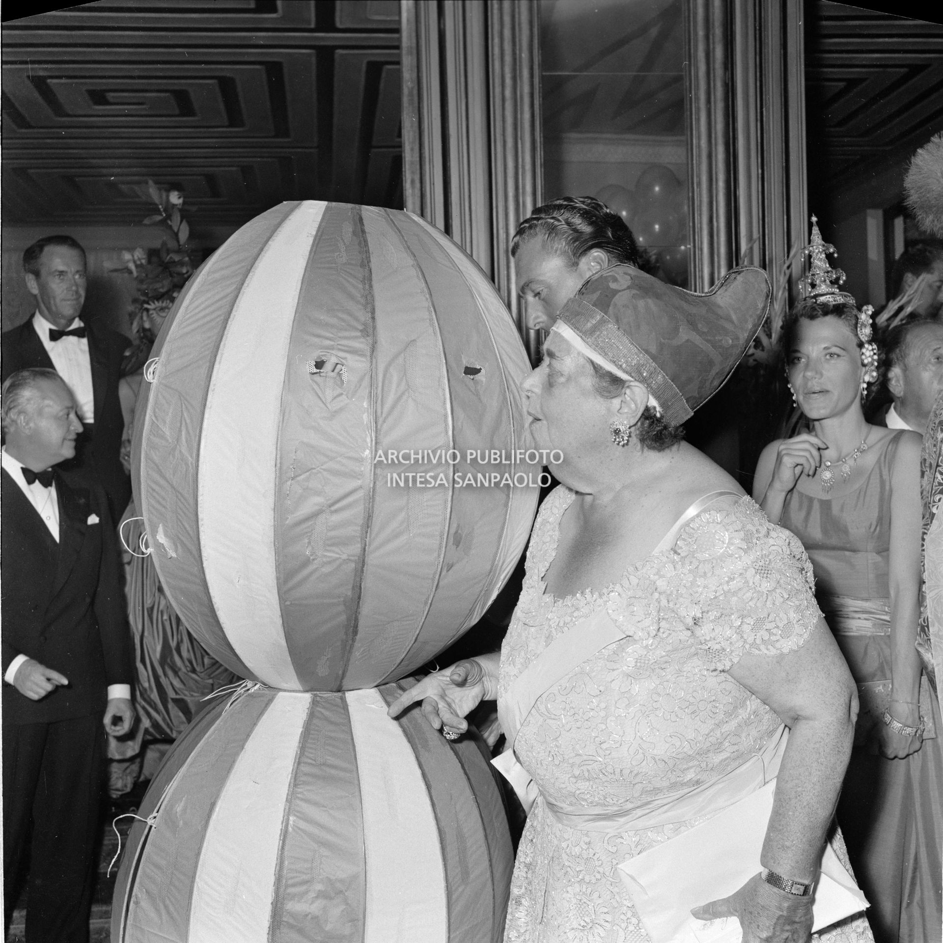 Elsa Maxwell sbircia nel curioso costume che avvolge Miss Maria Salata Philips al ricevimento organizzato dalla giornalista americana in onore di Maria Callas