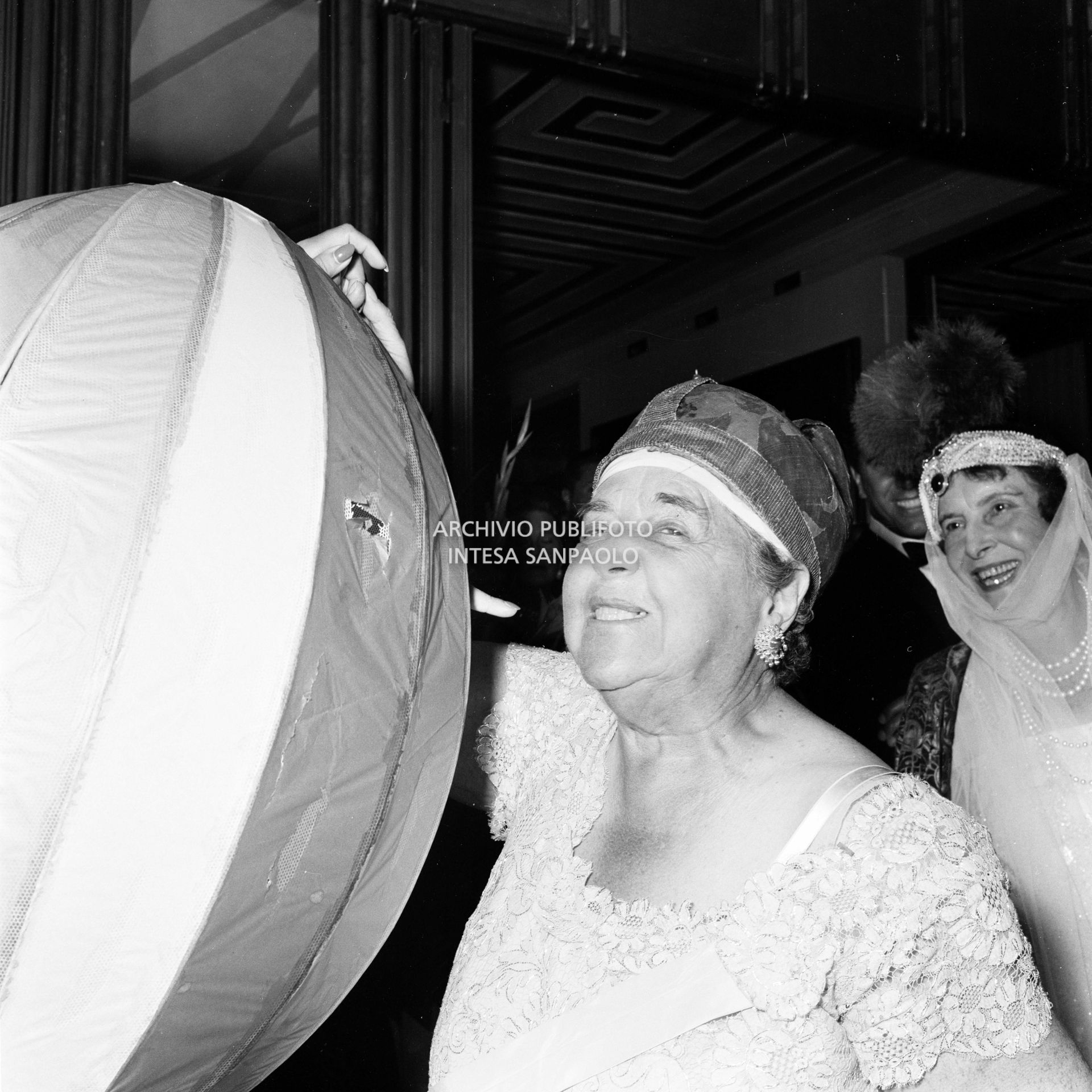 Elsa Maxwell sorride a fianco a Miss Maria Salata Philips avvolta da un curioso costume al ricevimento organizzato dalla giornalista americana in onore di Maria Callas