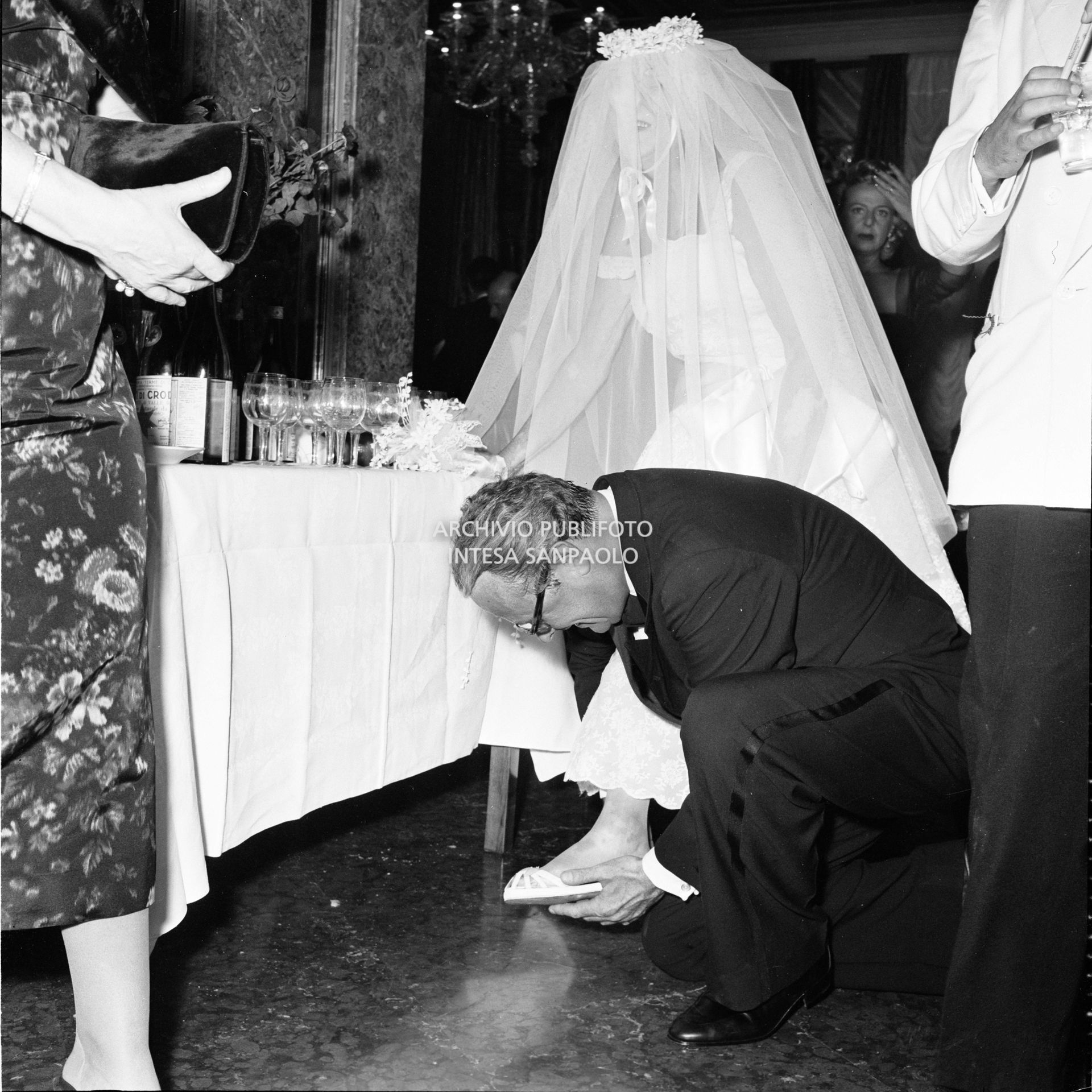 Un ospite del ricevimento organizzato da Elsa Maxwell in onore di Maria Callas sistema la calzatura alla baronessa Lillian Lo Monaco