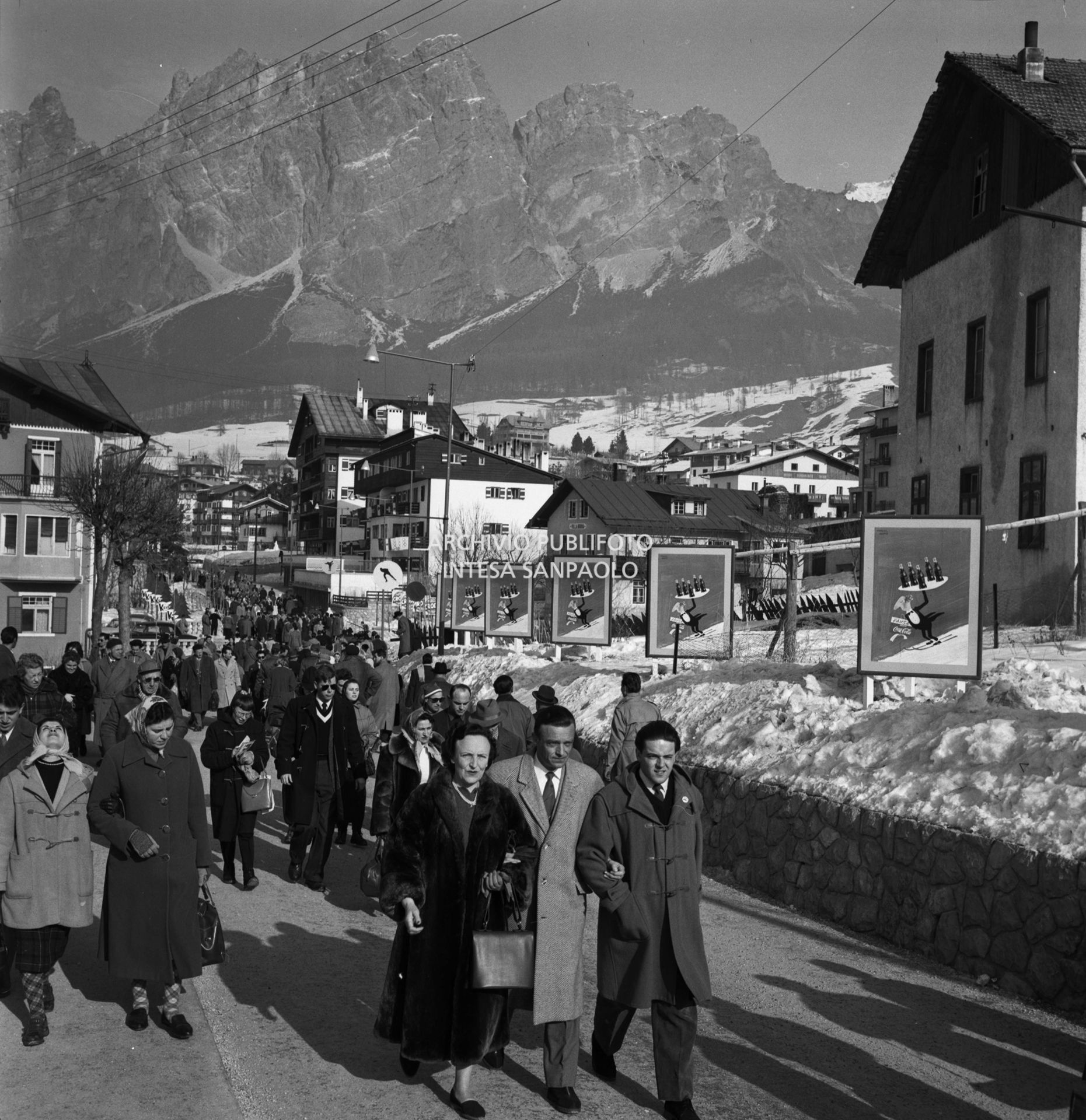 Cartelli pubblicitari dell'acqua e delle bibite Crodo lungo via del Castello, affollata di passanti, a Cortina d'Ampezzo nel periodo dei VII Giochi olimpici invernali