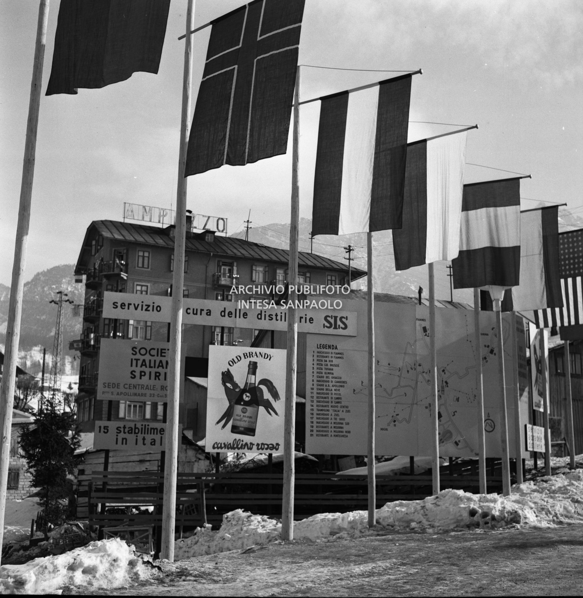 Cartelli pubblicitari della Società Italiana Spiriti, tra cui quella dell'Old Brandy Cavallino Rosso, esposti sotto le bandiere di varie nazionalità nei giorni dei VII Giochi olimpici invernali