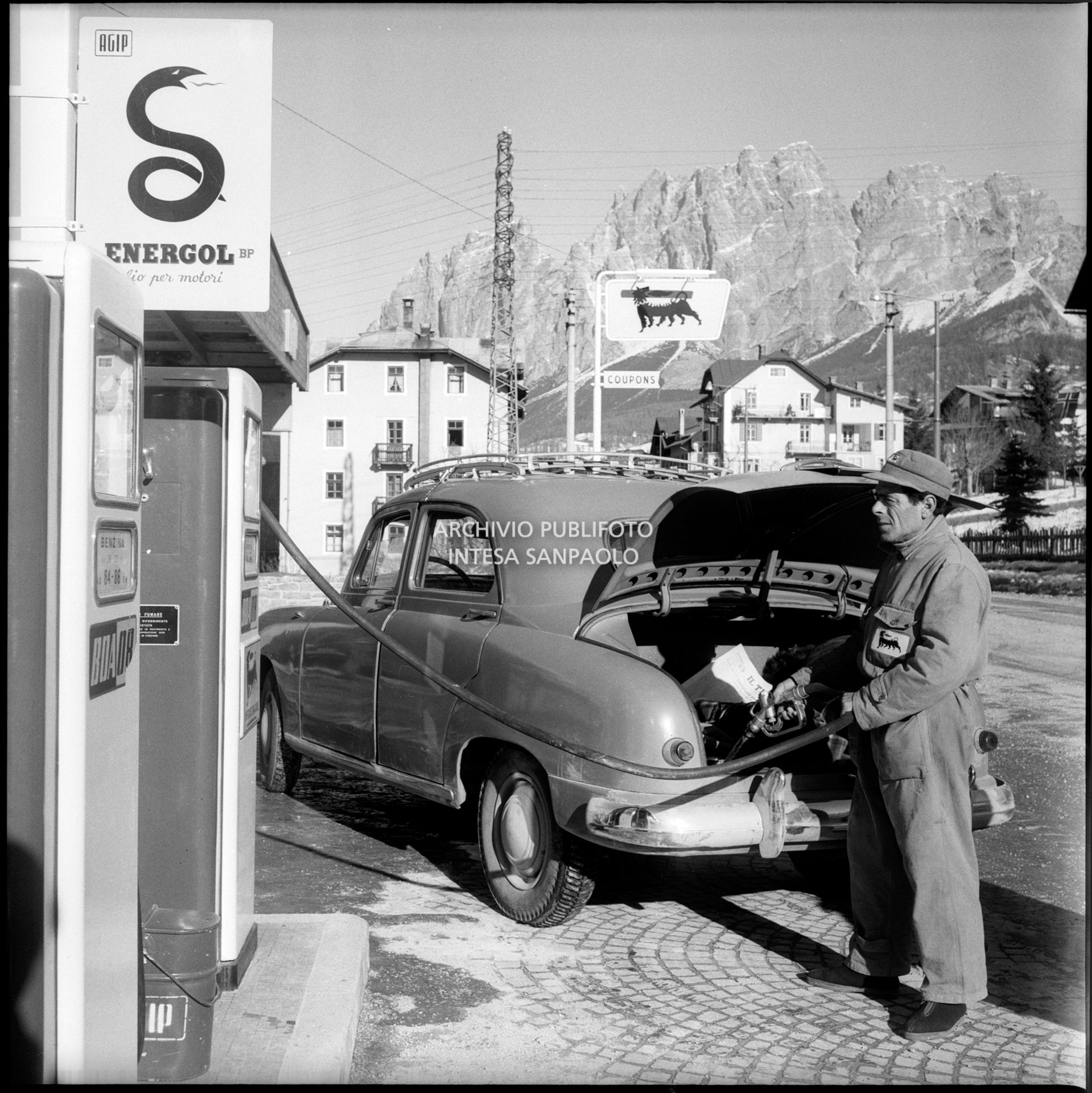 Una Fiat 1400 in rifornimento al distributore di carburante Agip presso una stazione di servizio nei pressi di Cortina d'Ampezzo nel periodo dei VII Giochi olimpici invernali
