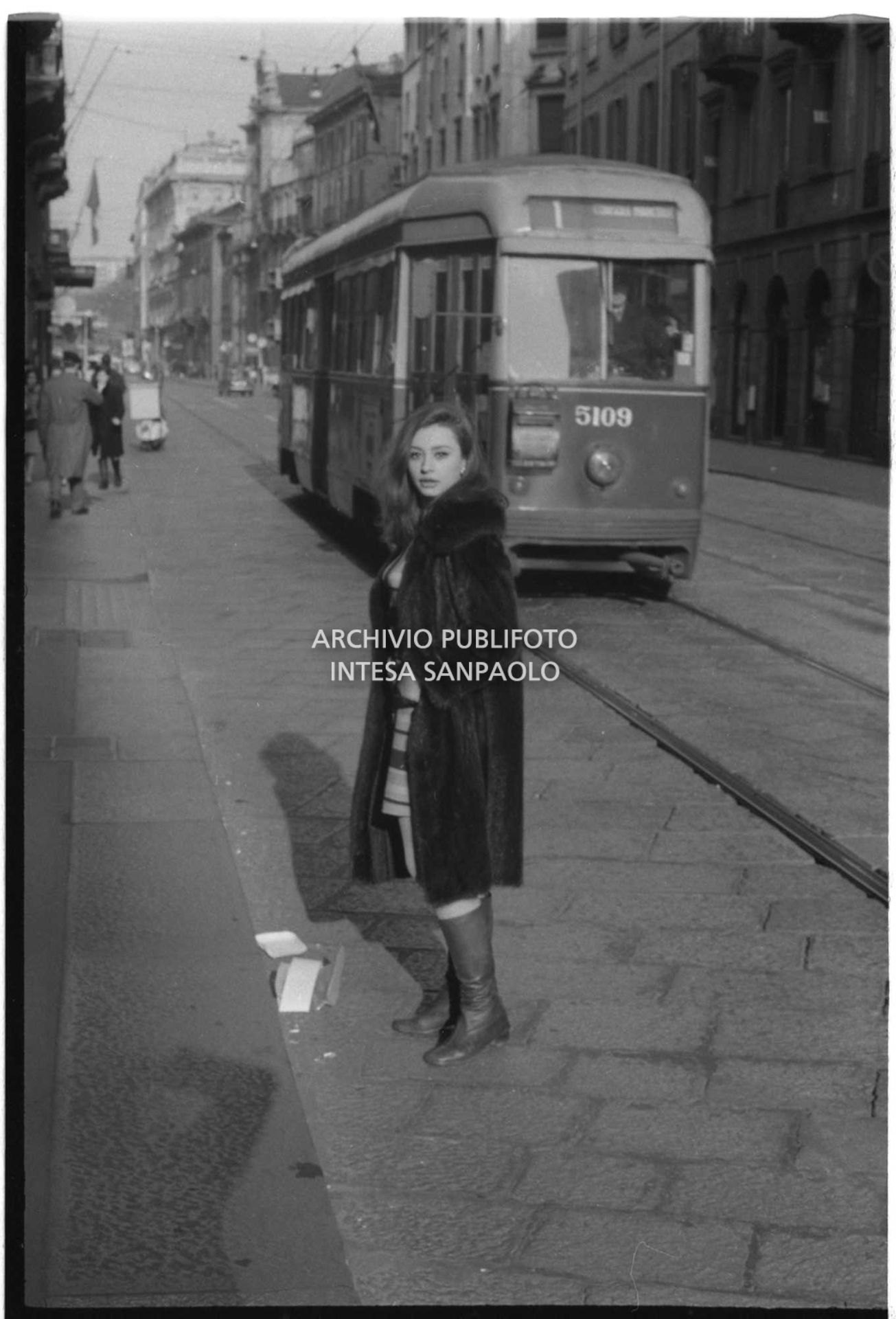 Raffaella Carrà in strada in via Manzoni; alle sue spalle transita un tram