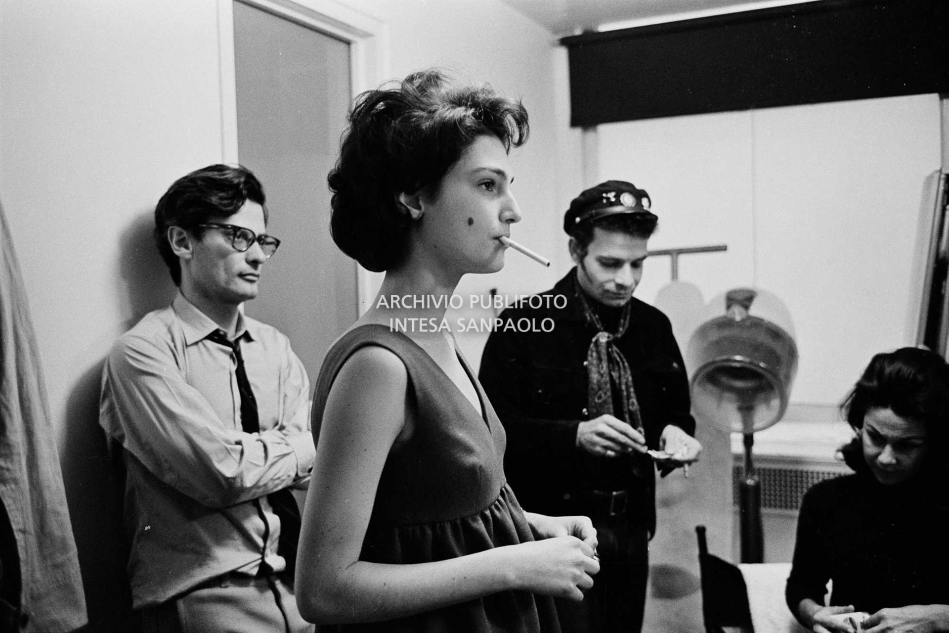 Benedetta Barzini in camerino con la sigaretta in bocca; alle sue spalle Richard Avedon, sullo sfondo due collaboratori