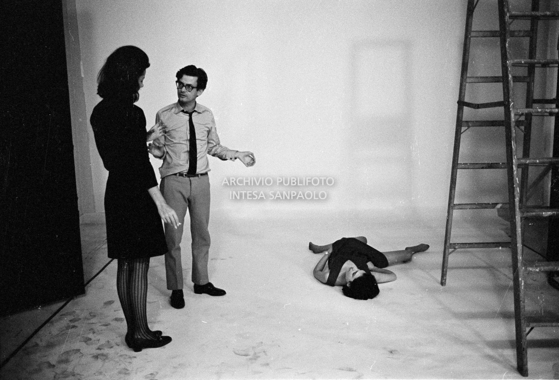 Set fotografico: Benedetta Barzini sdraiata in posa, Richard Avedon discorre con una collaboratrice