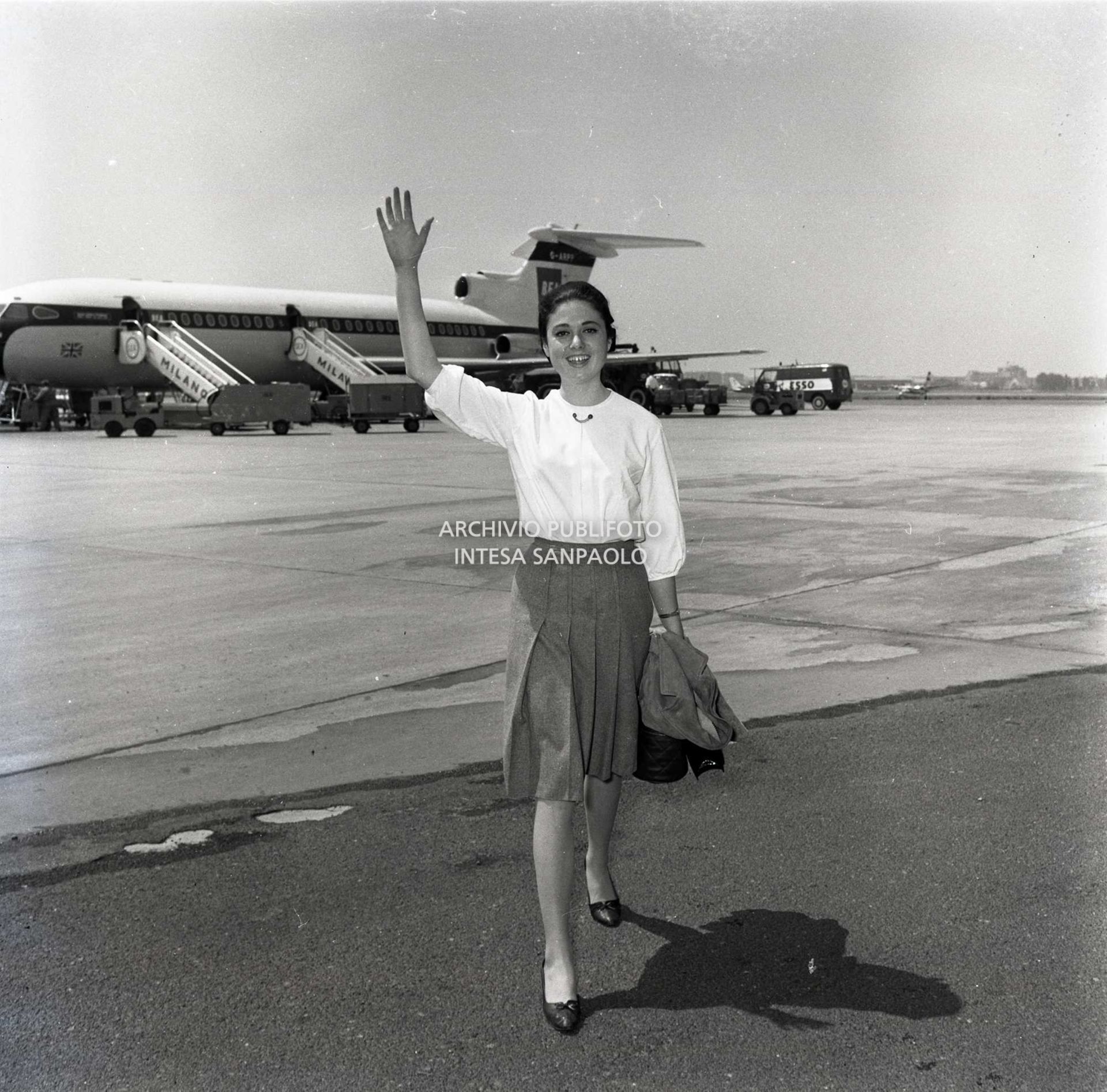 Gigliola Cinquetti saluta al suo arrivo all'aeroporto di Milano Linate; alle sue spalle un aeroplano in pista
