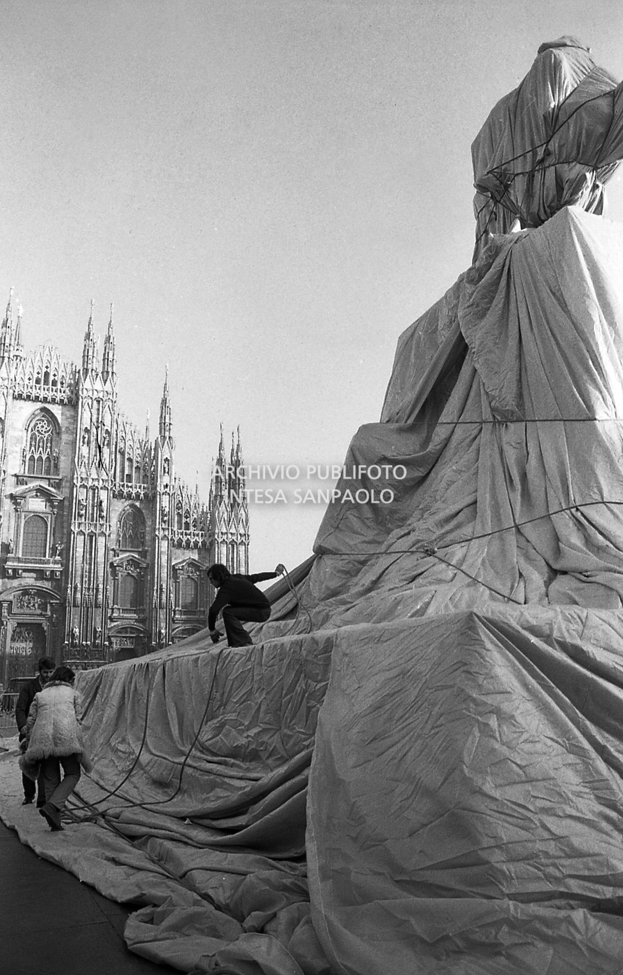 L'artista Christo mentre impacchetta la statua equestre di Re Vittorio Emanuele II in piazza del Duomo a Milano