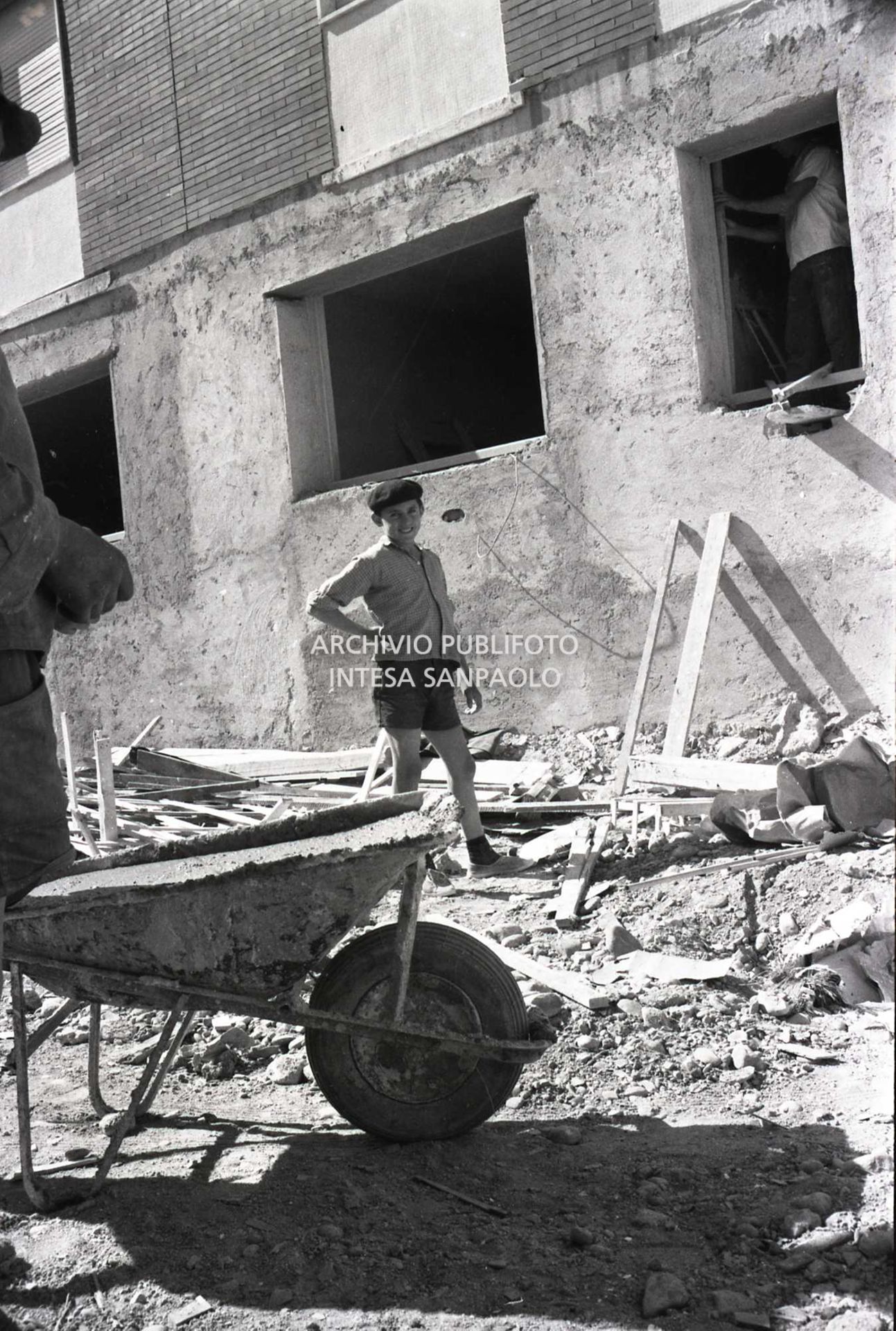 Ragazzino ritratto in un cantiere edile: in primo piano una carriola