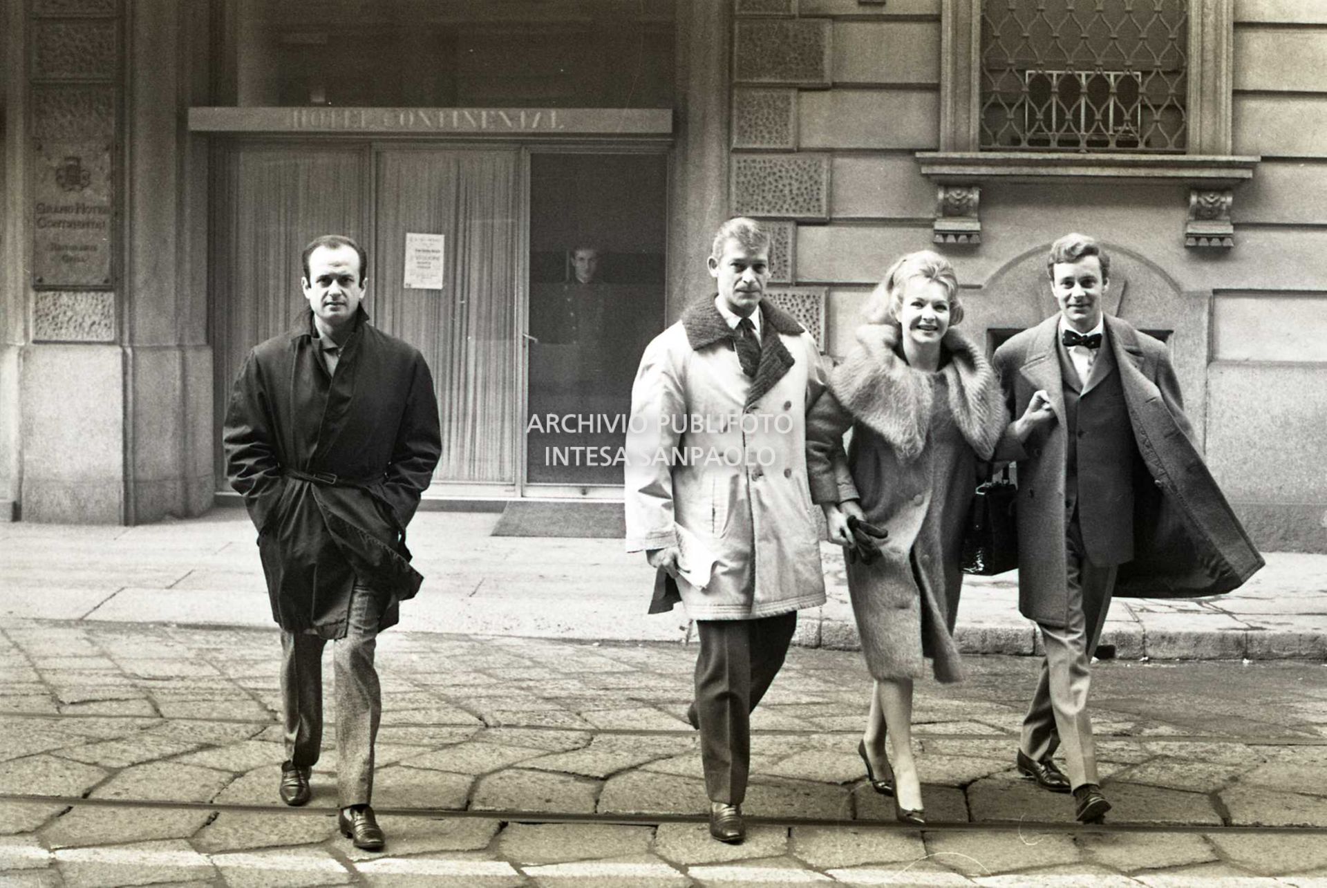 Line Renaud a braccetto con Paolo Poli (a destra) attraversa una via di Milano: sullo sfondo l'ingresso dell'Hotel Continental