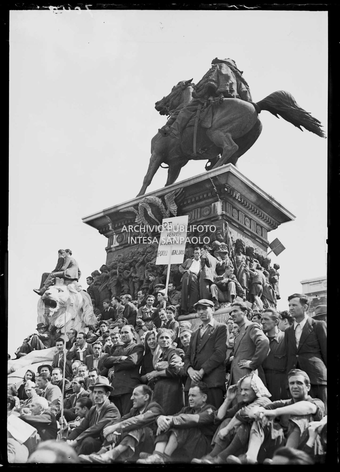 Folla seduta sulla base del monumento a Vittorio Emanuele II in piazza del Duomo a Milano alla manifestazione anti-monarchica