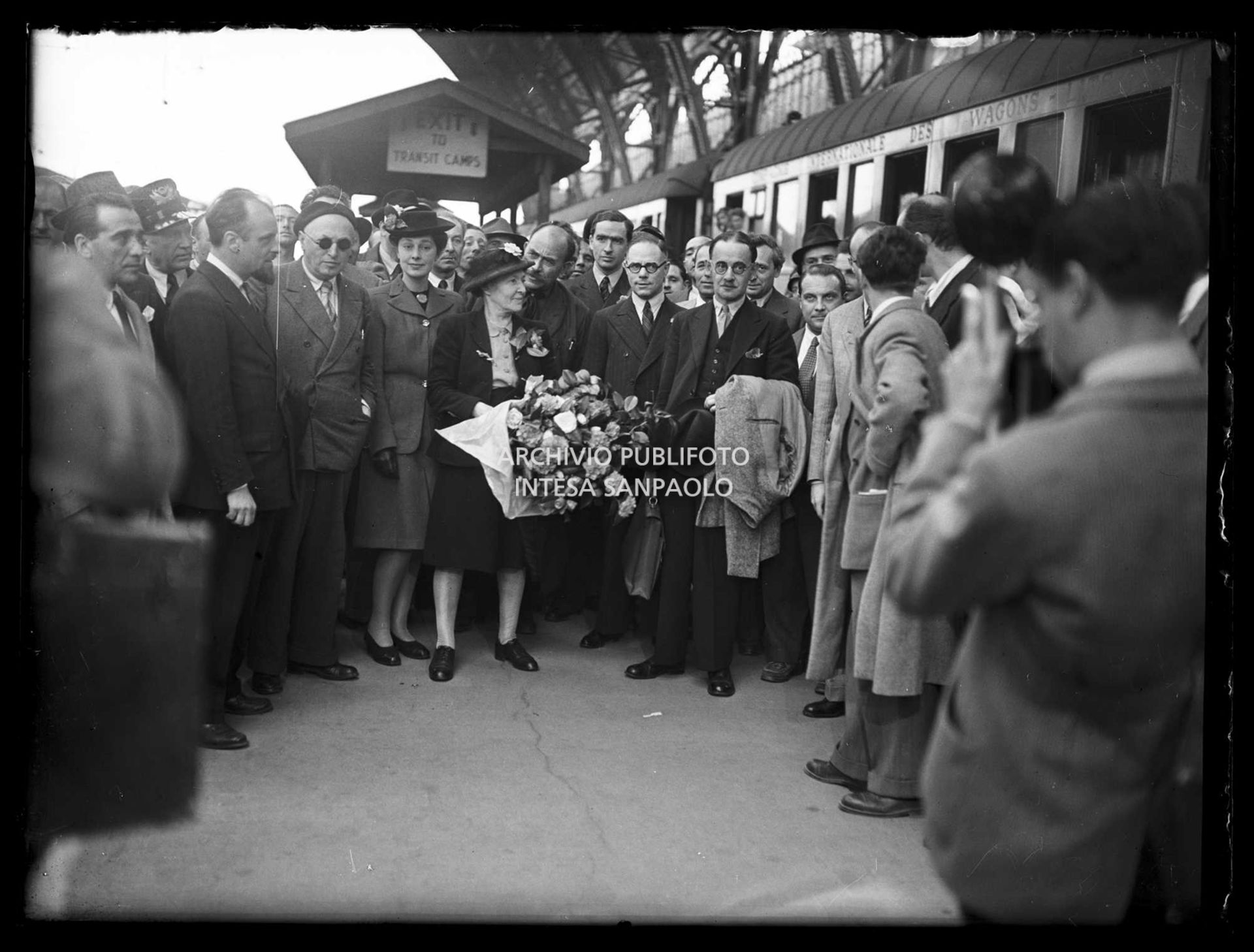 Harold Laski (a destra con il soprabito sul braccio), presidente del Partito laburista inglese, appena arrivato a Milano con Frida Kerry, sua moglie (al centro con i fiori), accolti da Pietro Nenni (a sinistra con gli occhiali da sole)