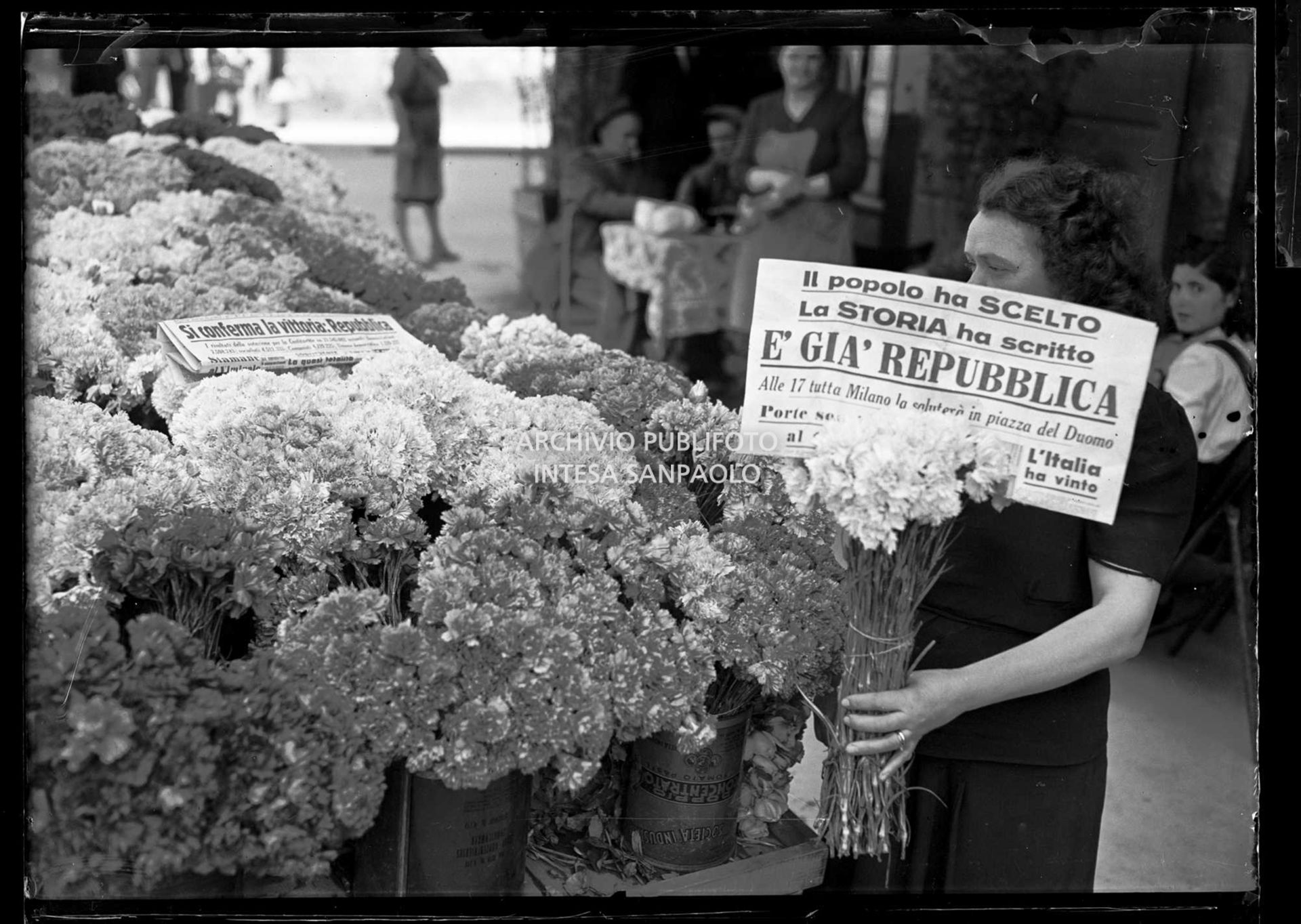 Una fioraia tiene in mano un mazzo di fiori e il quotidiano Milano-Sera che titola: "Il popolo ha scelto. La storia ha scritto. È già Repubblica"