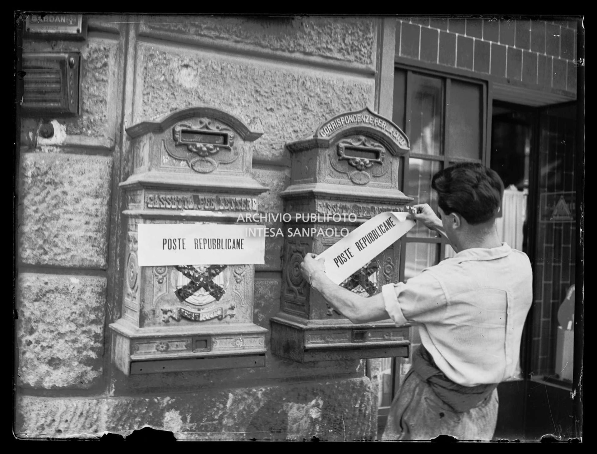 Un uomo affigge sulle cassette per lettere la scritta: "Poste repubblicane" sopra lo stemma monarchico