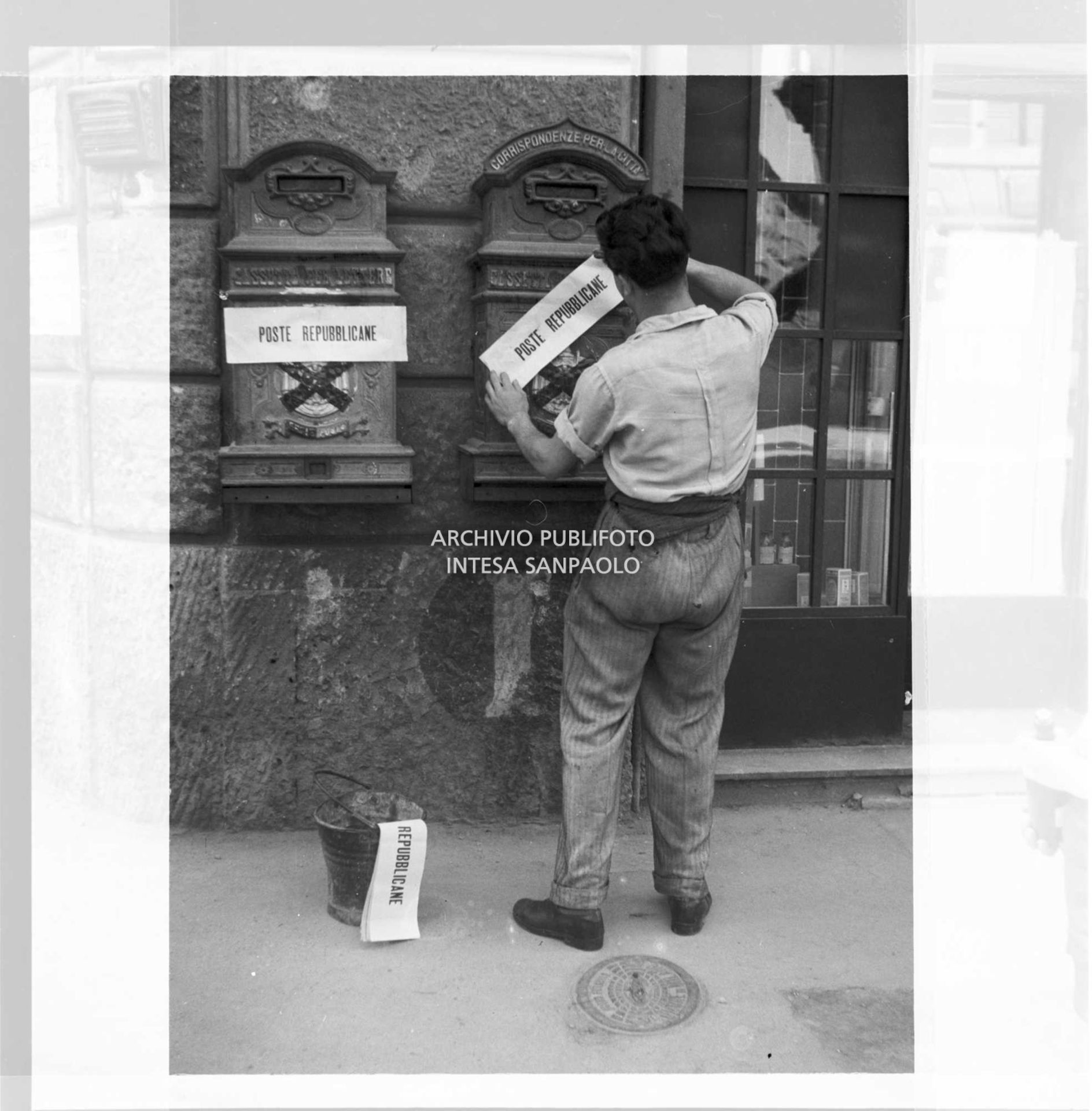 Un uomo affigge sulle cassette per lettere la scritta: "Poste repubblicane" sopra lo stemma monarchico