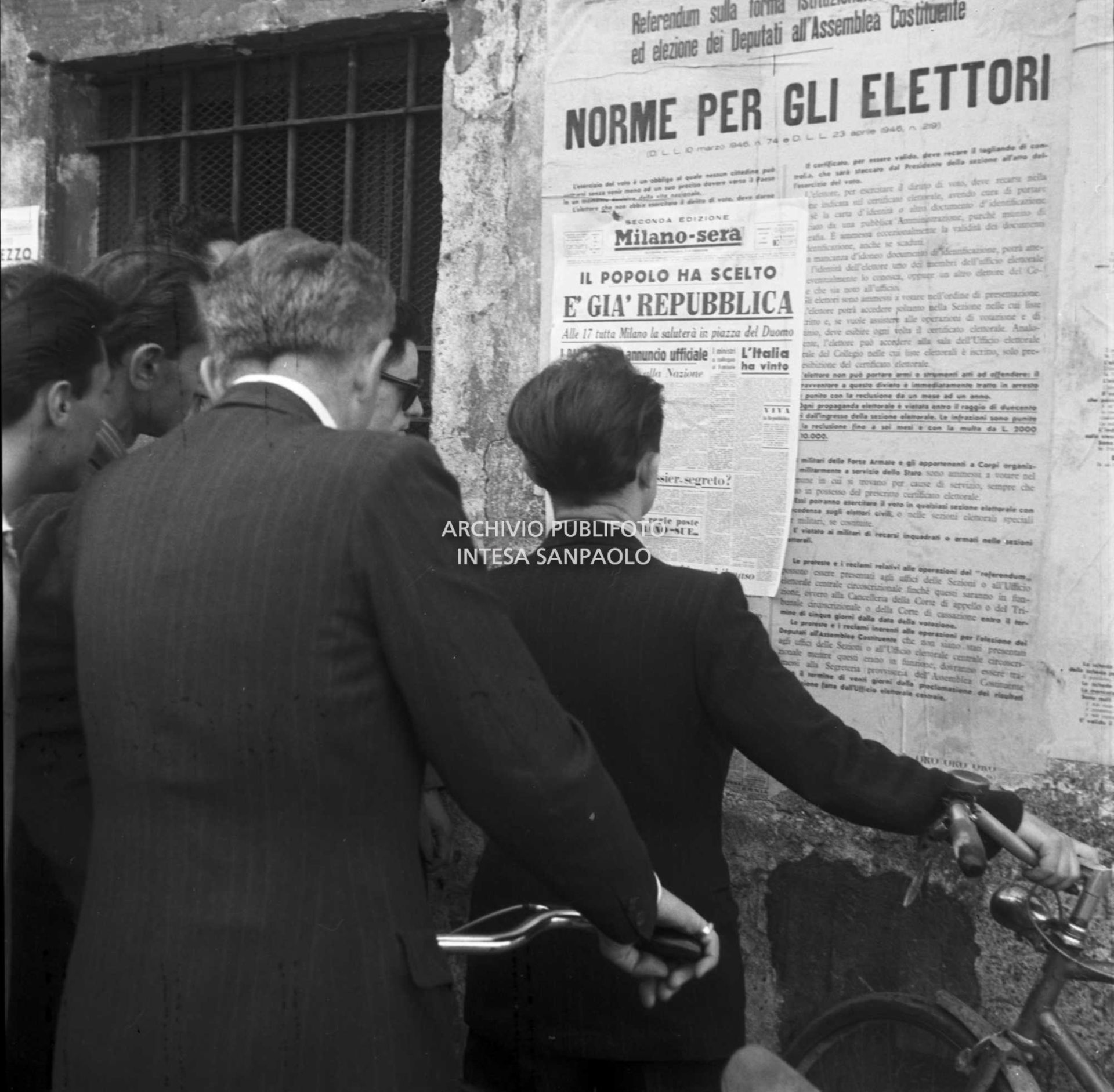 Passanti per strada leggono la prima pagina della seconda edizione del quotidiano Milano-Sera, affissa a un muro, che titola: "Il popolo ha scelto. È già Repubblica"