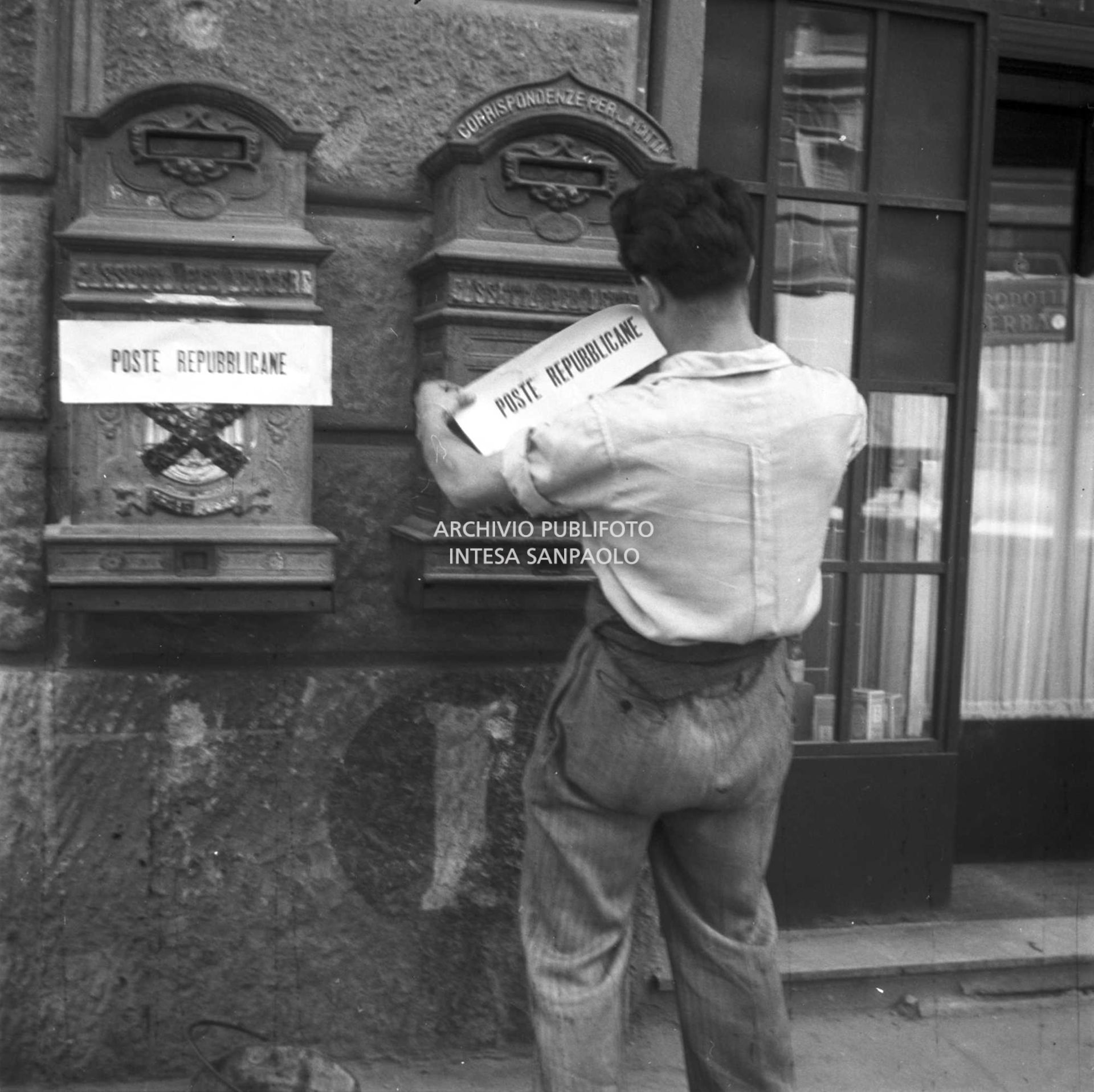 Un uomo affigge sulle cassette per lettere la scritta: "Poste repubblicane" sopra lo stemma monarchico