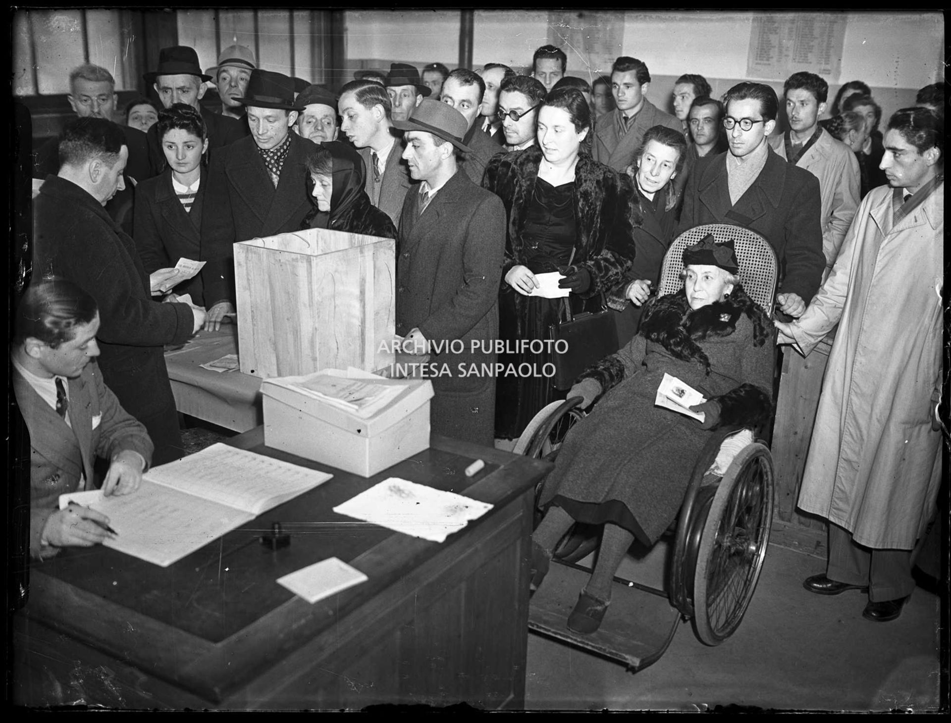 Cittadini al voto al seggio in occasione delle elezioni comunali a Saronno, le prime elezioni a suffragio universale in Italia; in primo piano una anziana donna in sedia a rotelle