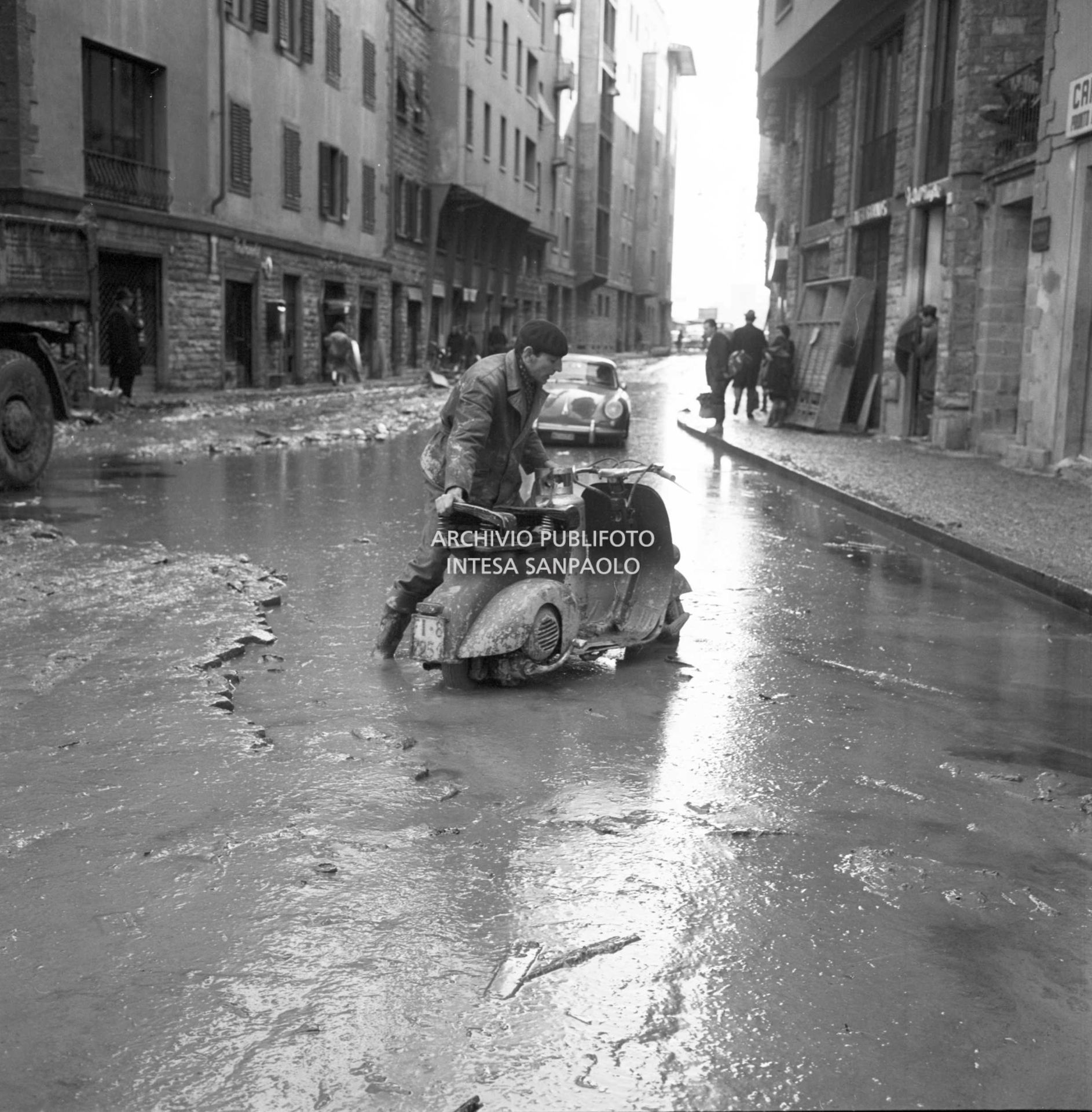 Alluvione di Firenze: un uomo spinge una Vespa, con a bordo una bombola di gas, nelle strade invase dal fango, dopo lo straripamento del fiume Arno