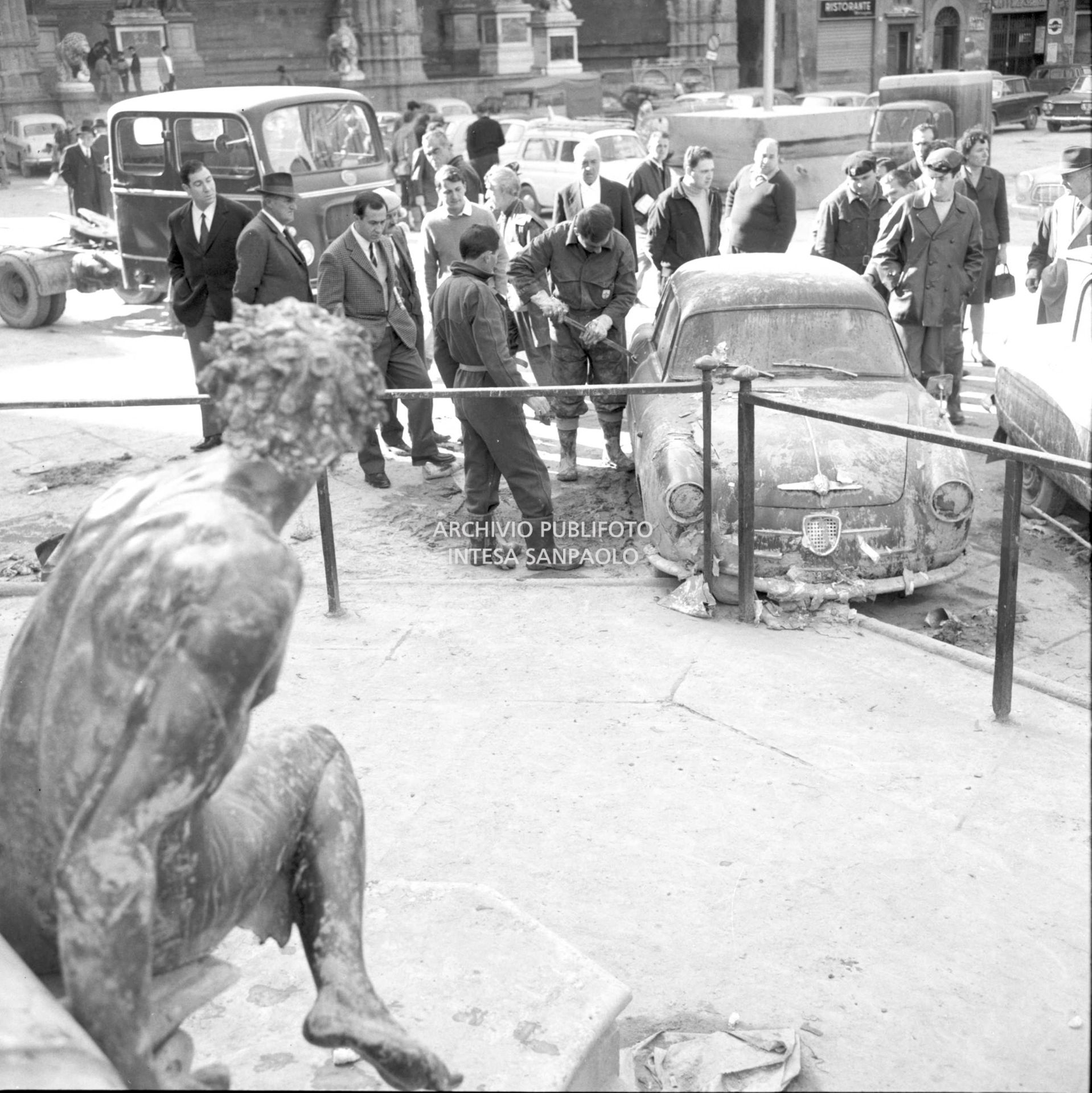 Alluvione di Firenze: un gruppo di persone intorno a una Fiat 600 Berlinetta Monterosa infangata e danneggiata, in piazza della Signoria, a ridosso della fontana di Nettuno
